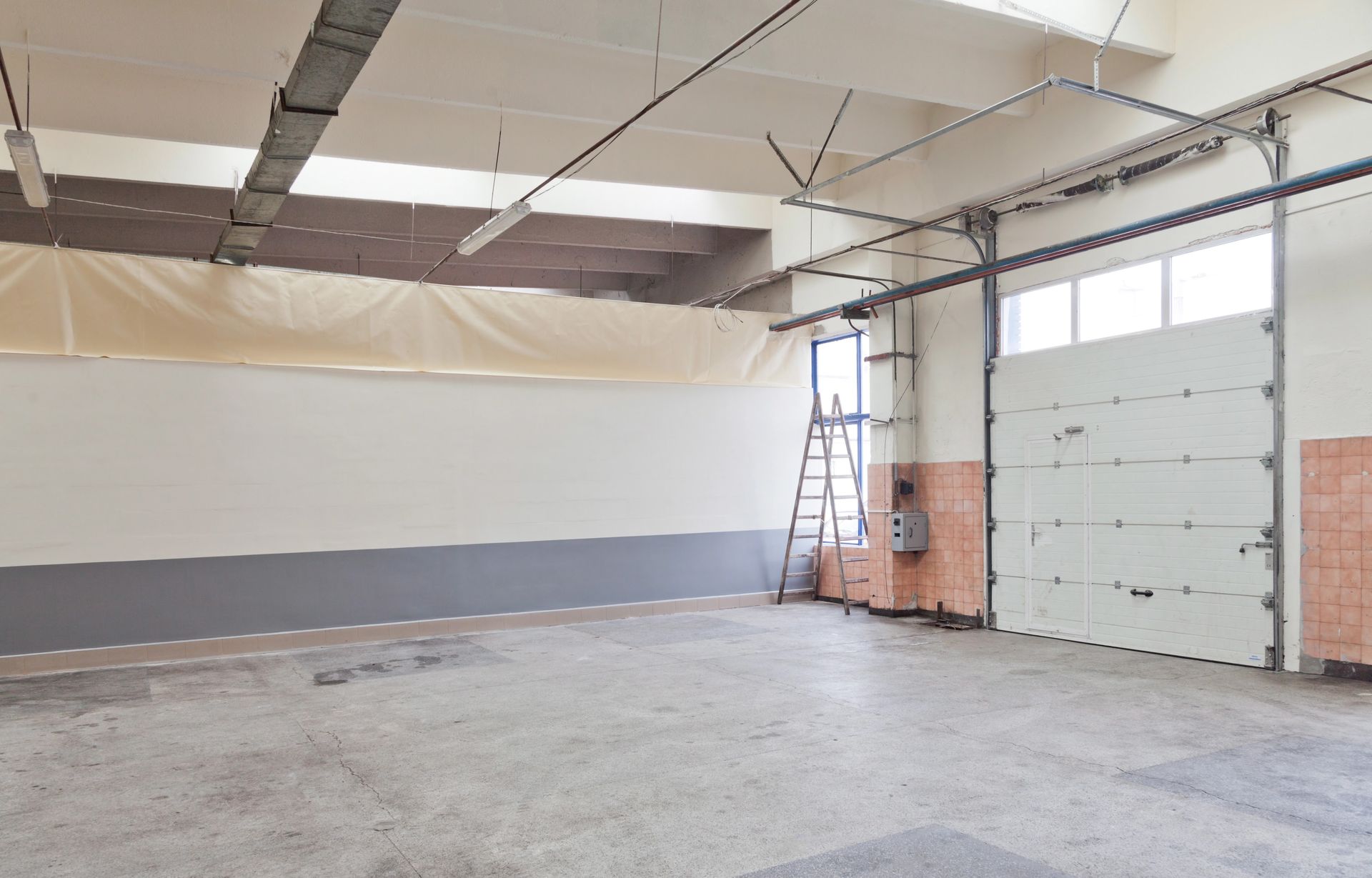 Empty warehouse interior with concrete floor, white walls, and large garage door openings