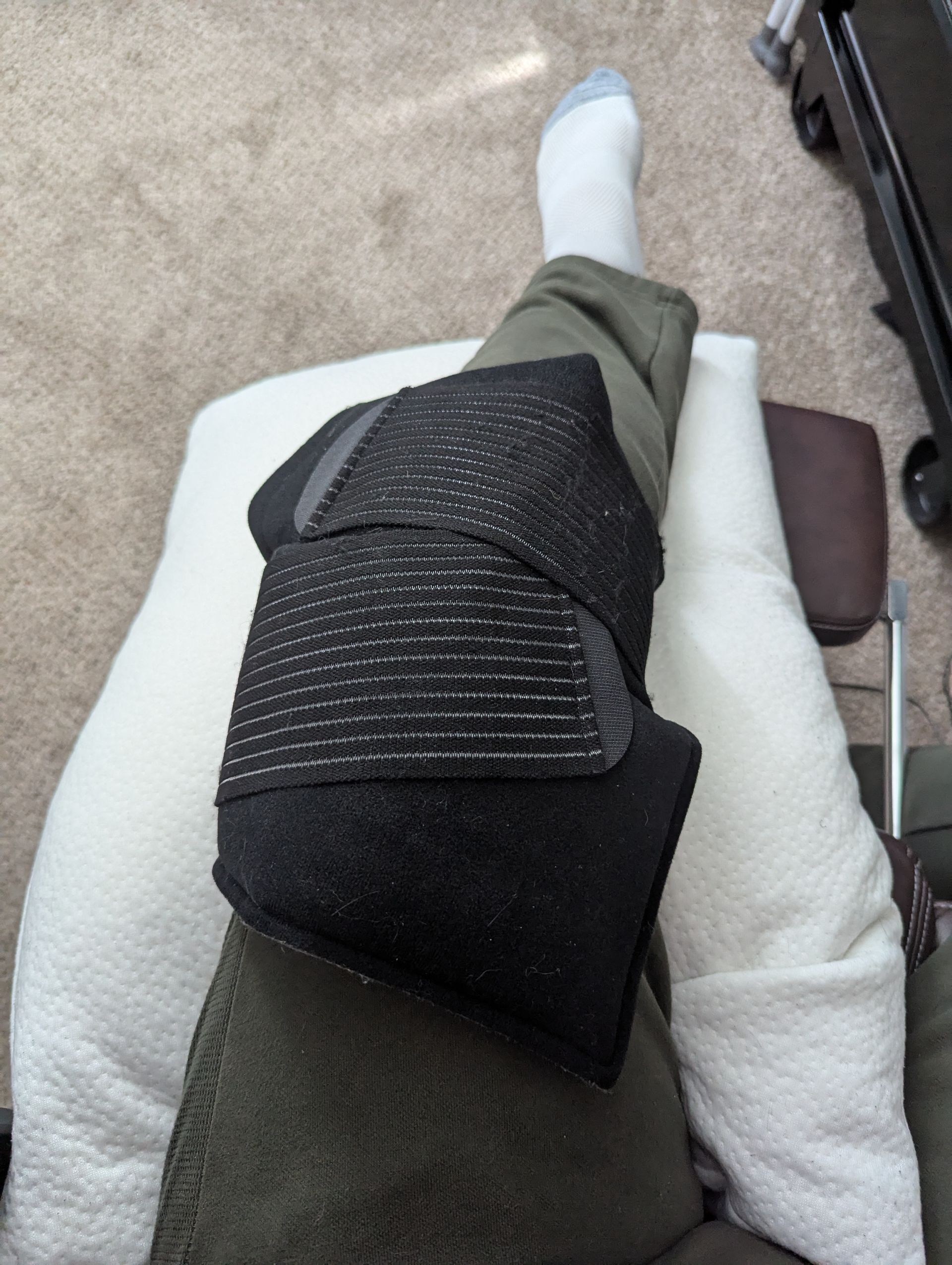 A person is sitting on a couch with a black knee brace on their leg.