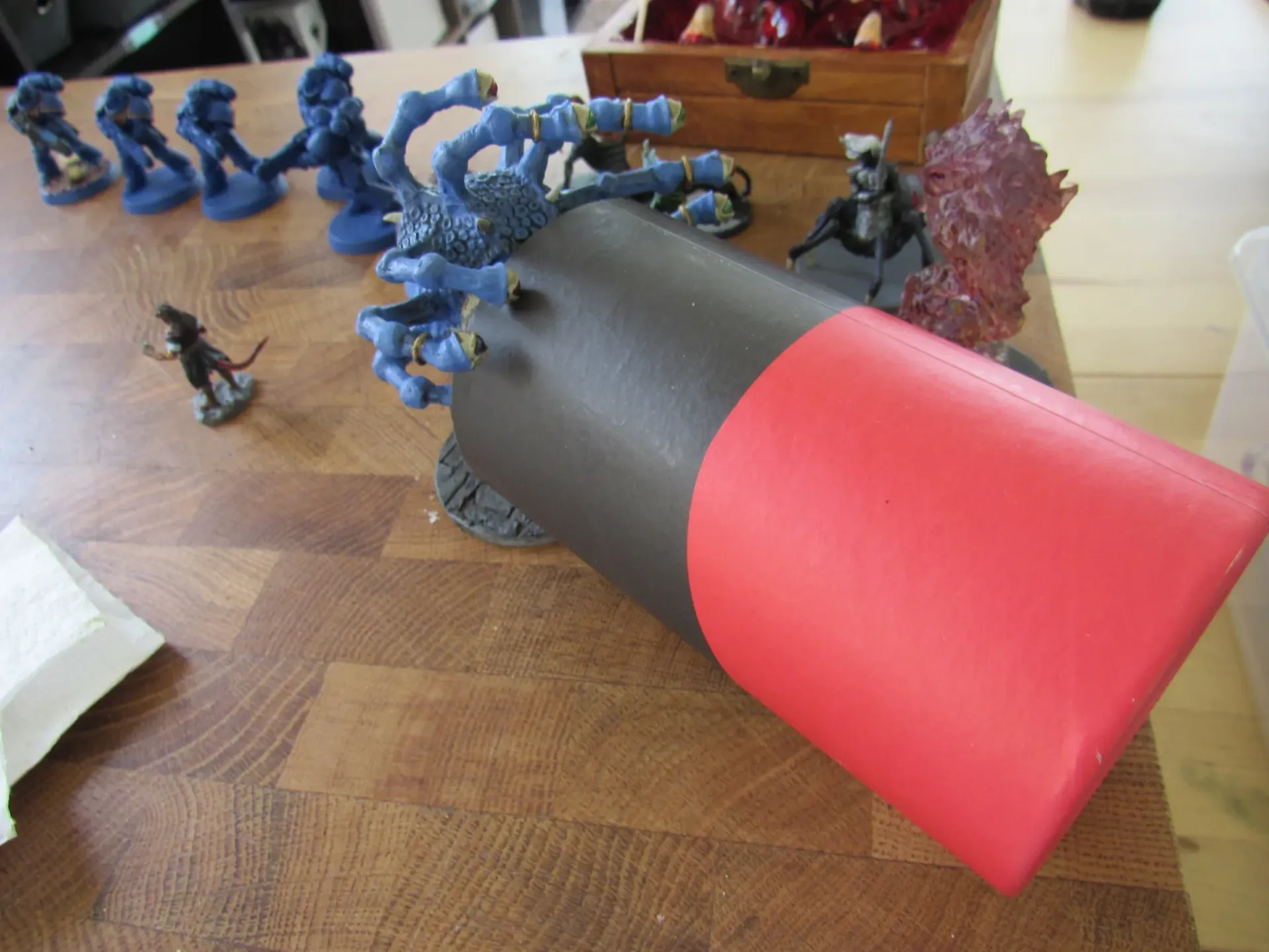 Miniature figures surround a black and red foam structure on a wooden surface.