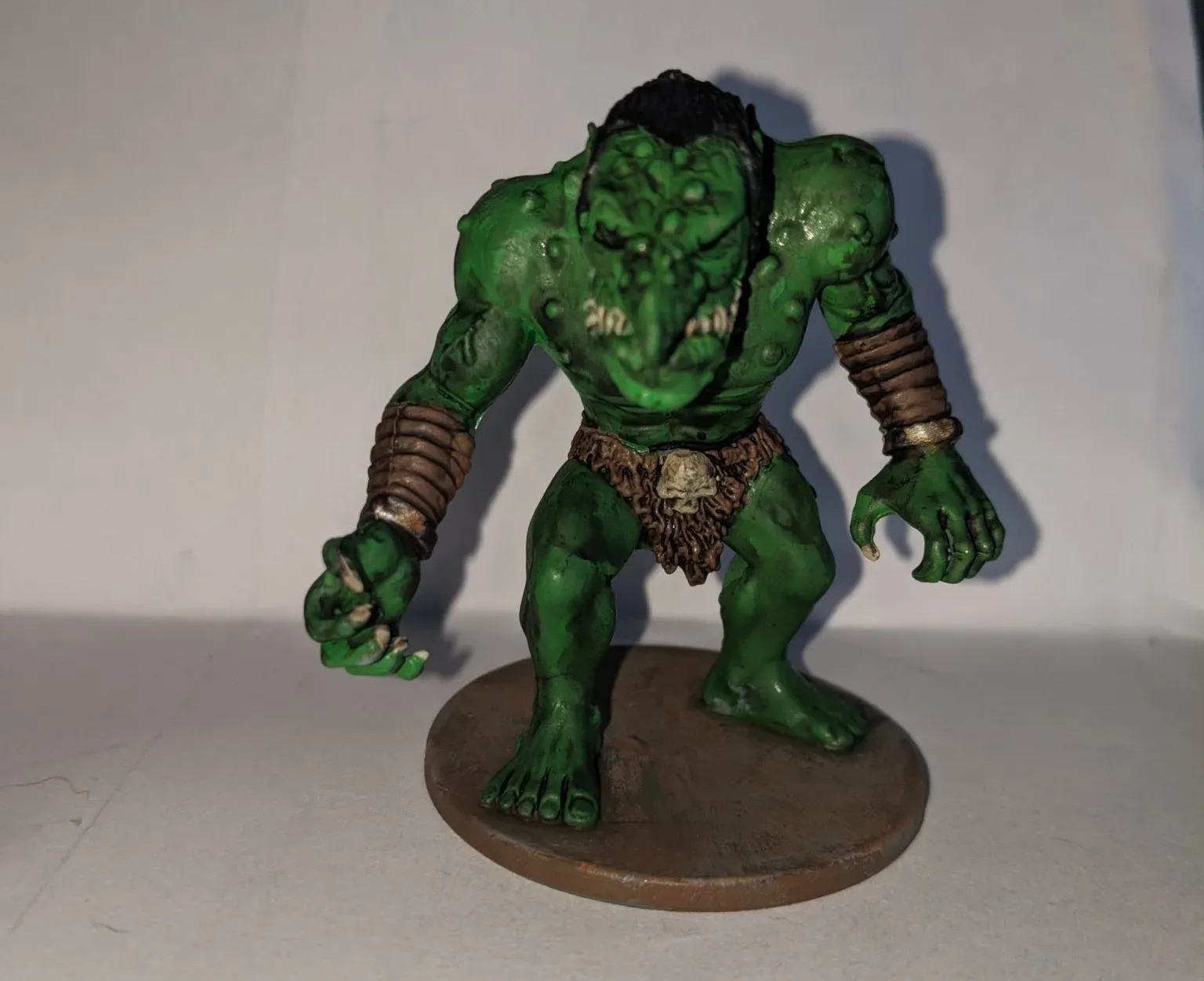 Green ogre figurine on a brown base; green skin, black hair, and leather armbands.