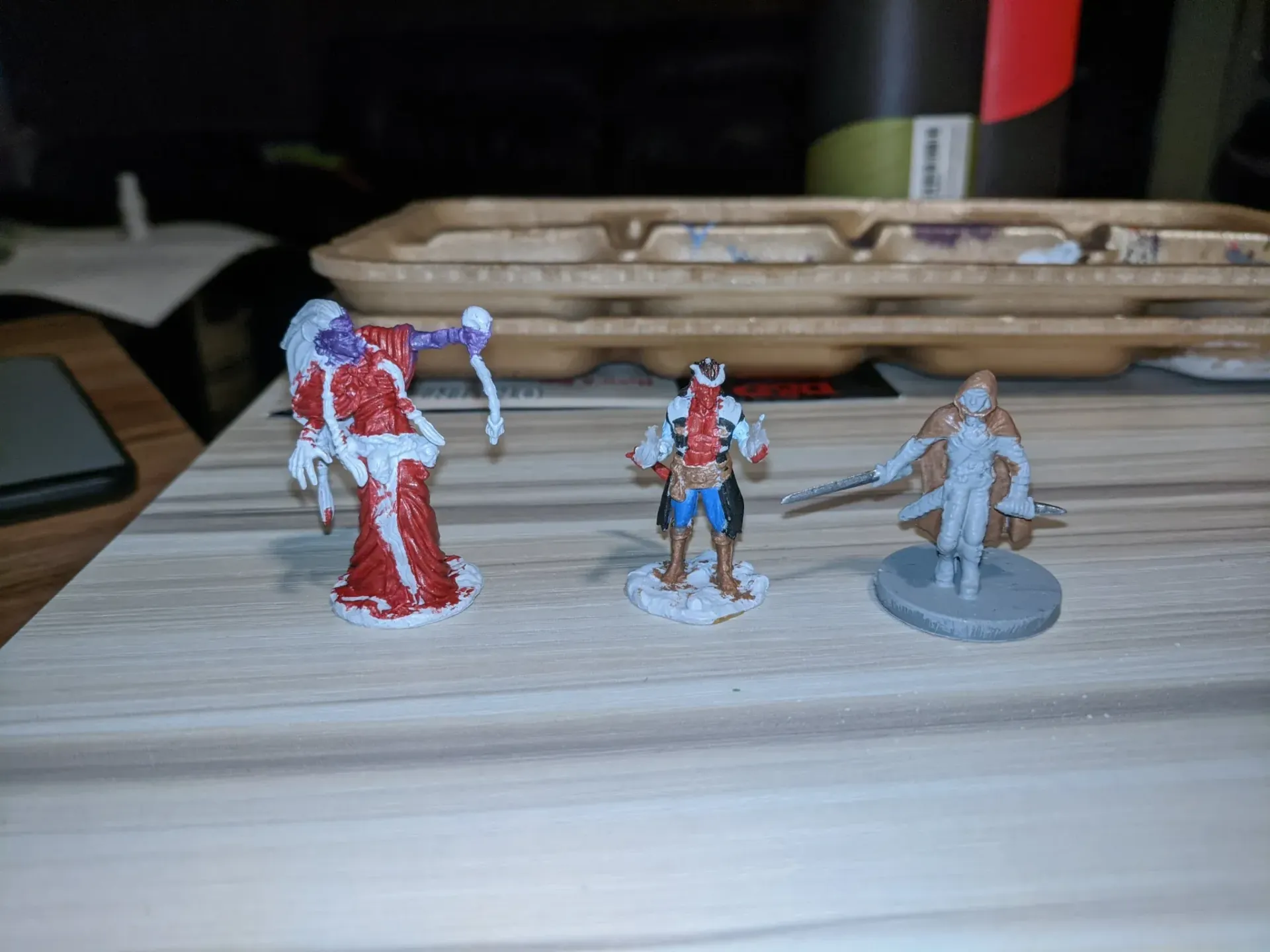 Three painted fantasy miniatures on a table: a ghoul in red, a pirate, and a robed figure.