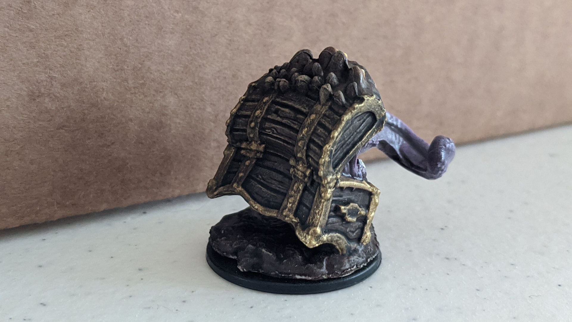 Miniature monster figure, dark black with gold accents and a purple tentacle, on a rocky base.