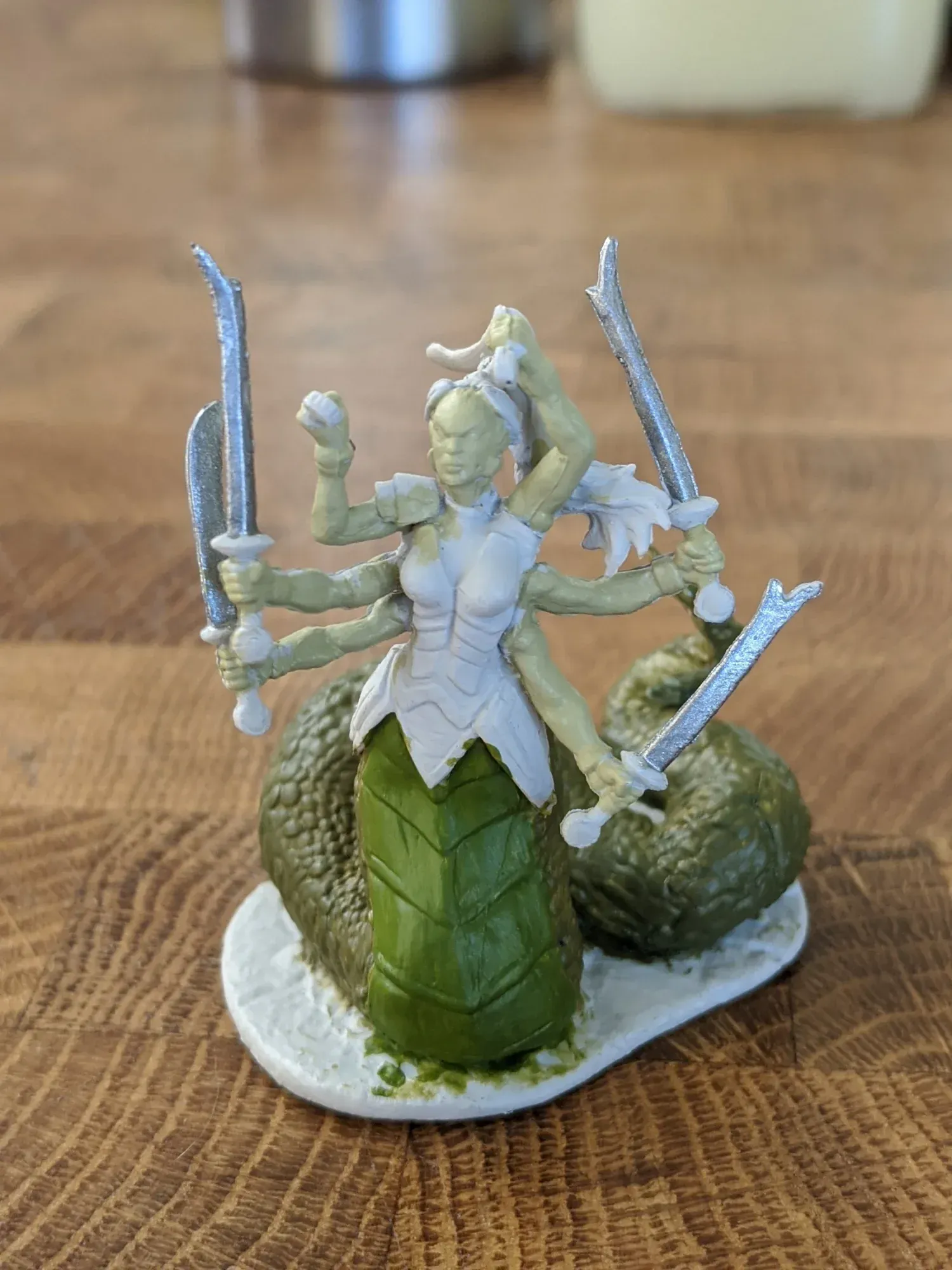 A miniature multi-armed serpent-like humanoid holding swords, on a rocky base.