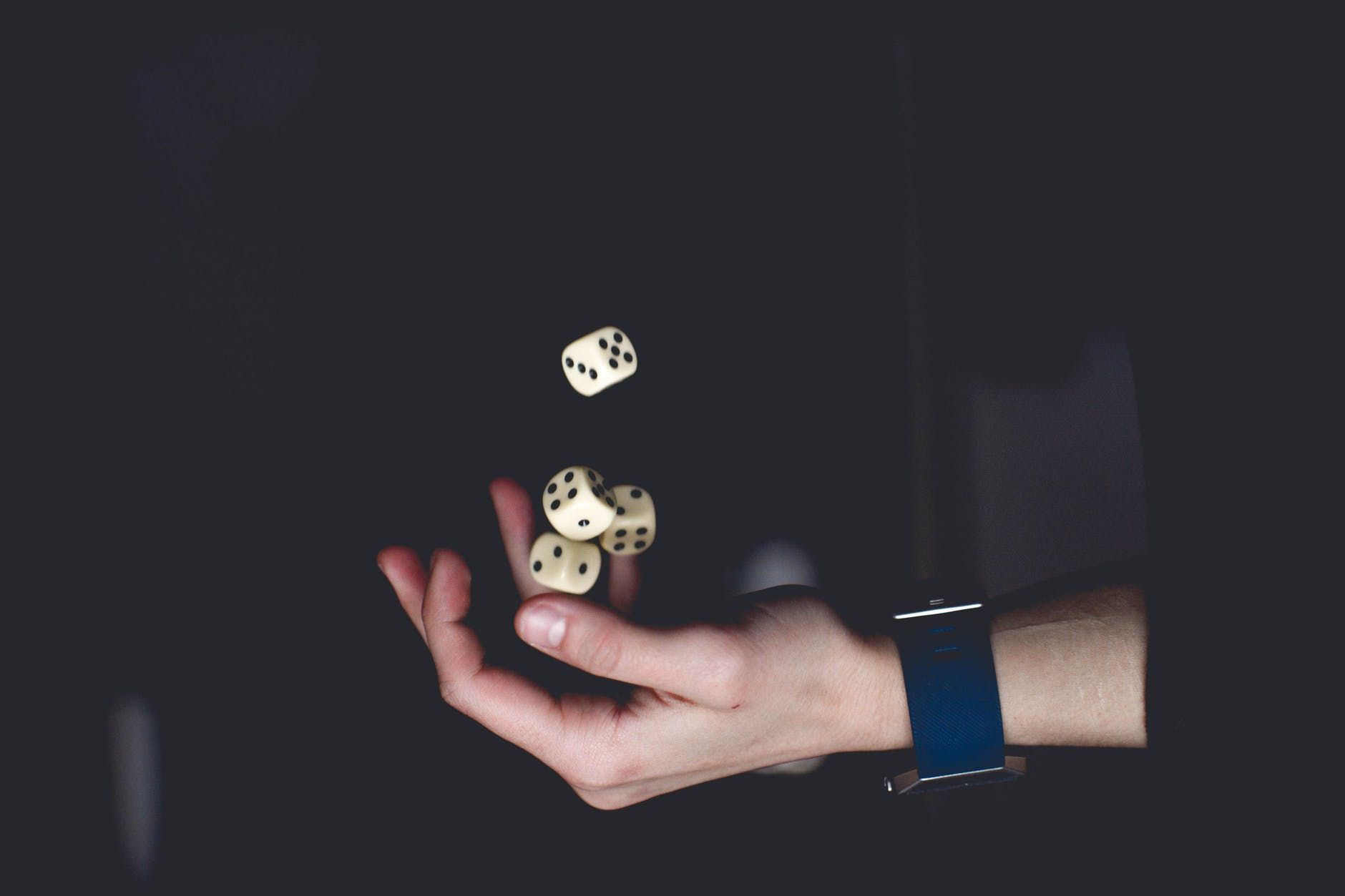 Hand tossing dice in the air against a dark background, wrist with blue watch visible.