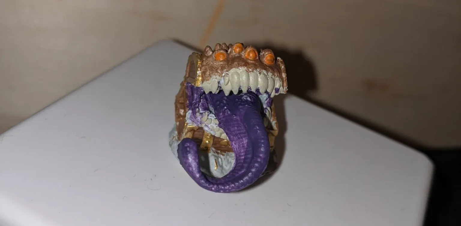 A detailed close-up of a purple and gold monster ring. White teeth and a purple tongue are visible.