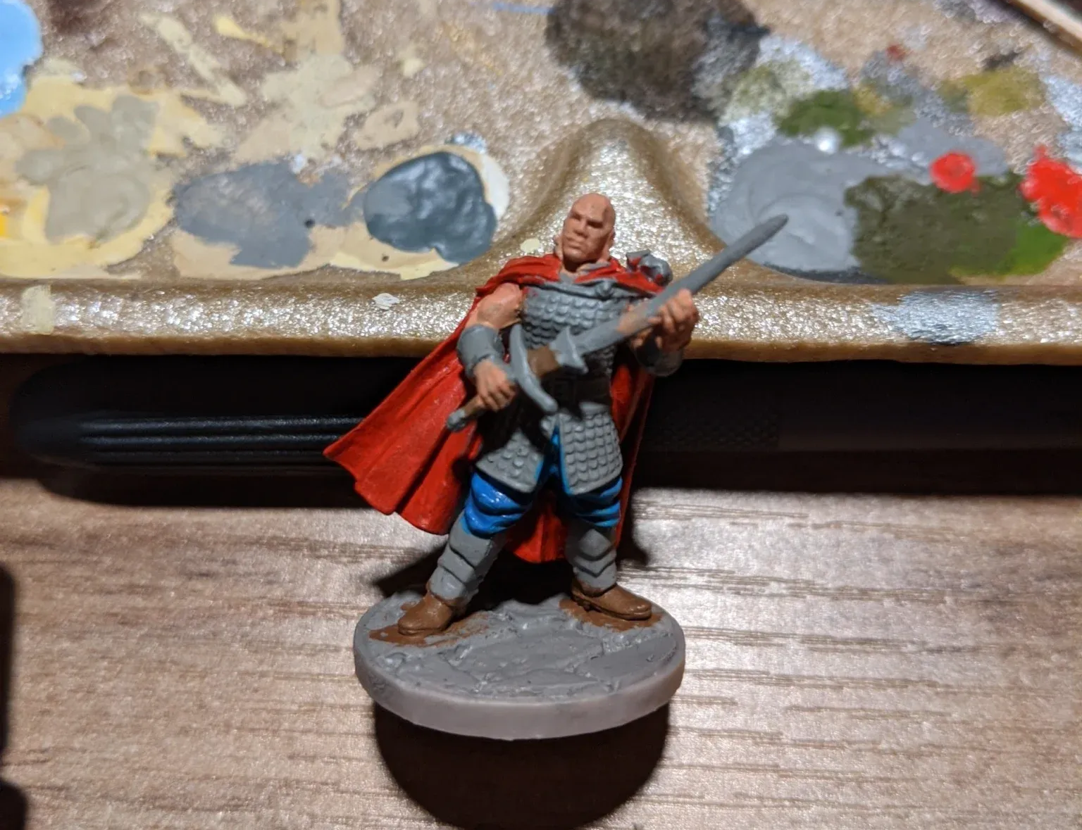 Miniature warrior in red cape, chainmail, and blue pants, holding a sword.
