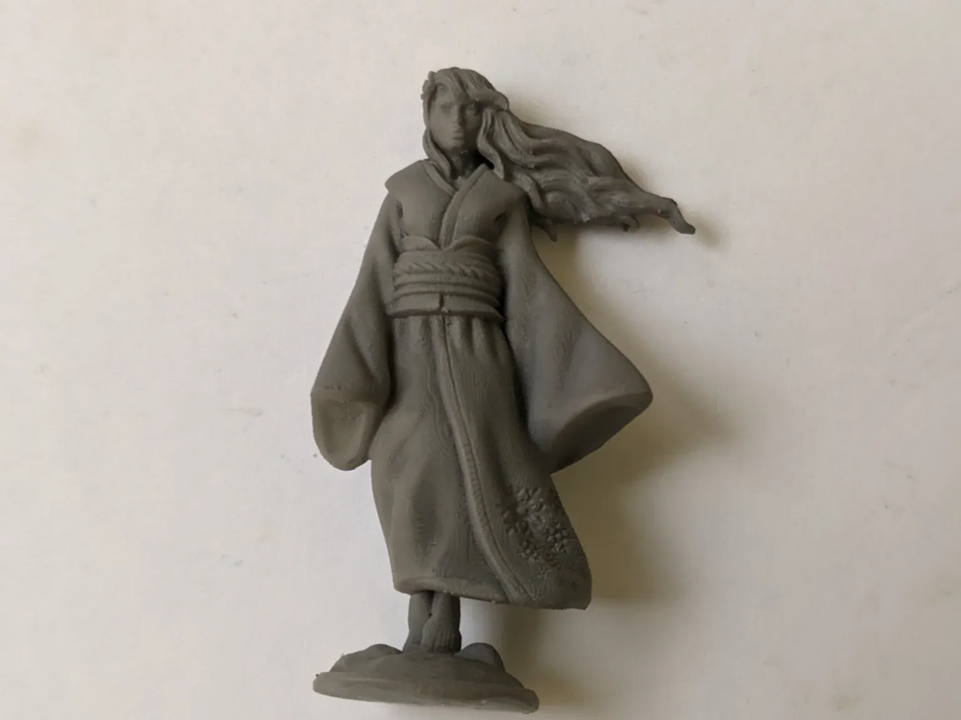 A grey clay figurine of a woman in a robe with long flowing hair.