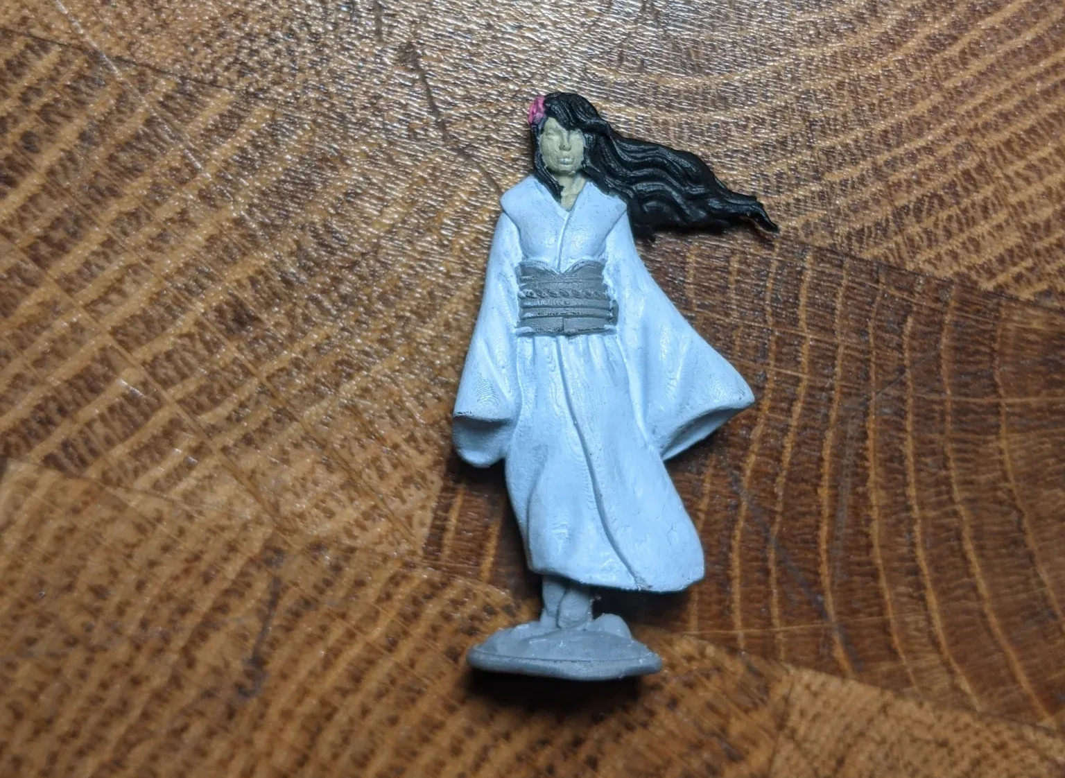 Miniature figure of a woman in a white kimono with long black hair, a pink flower, and gray details.