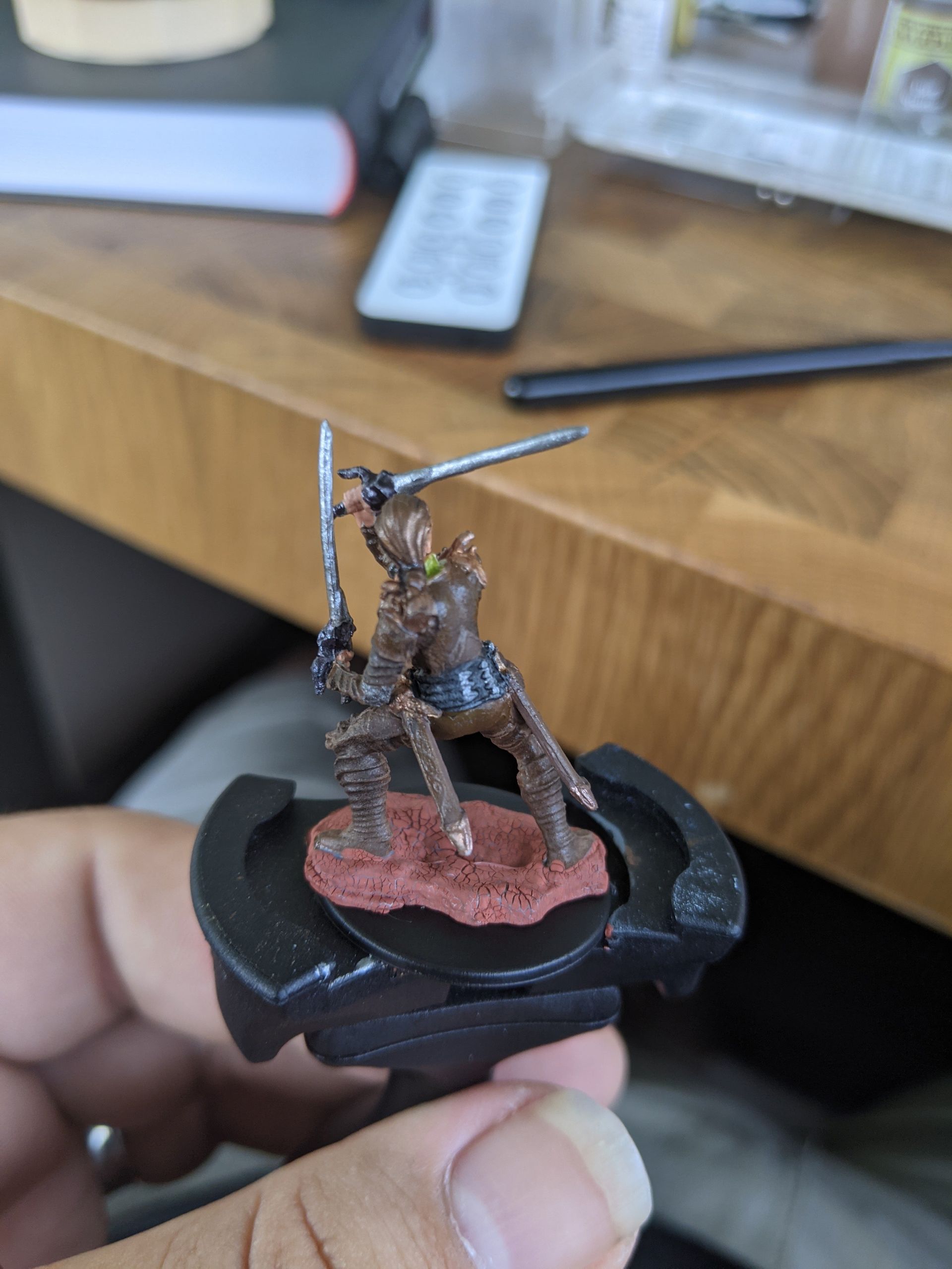 Miniature figure of a warrior in brown armor with two swords on a black base.