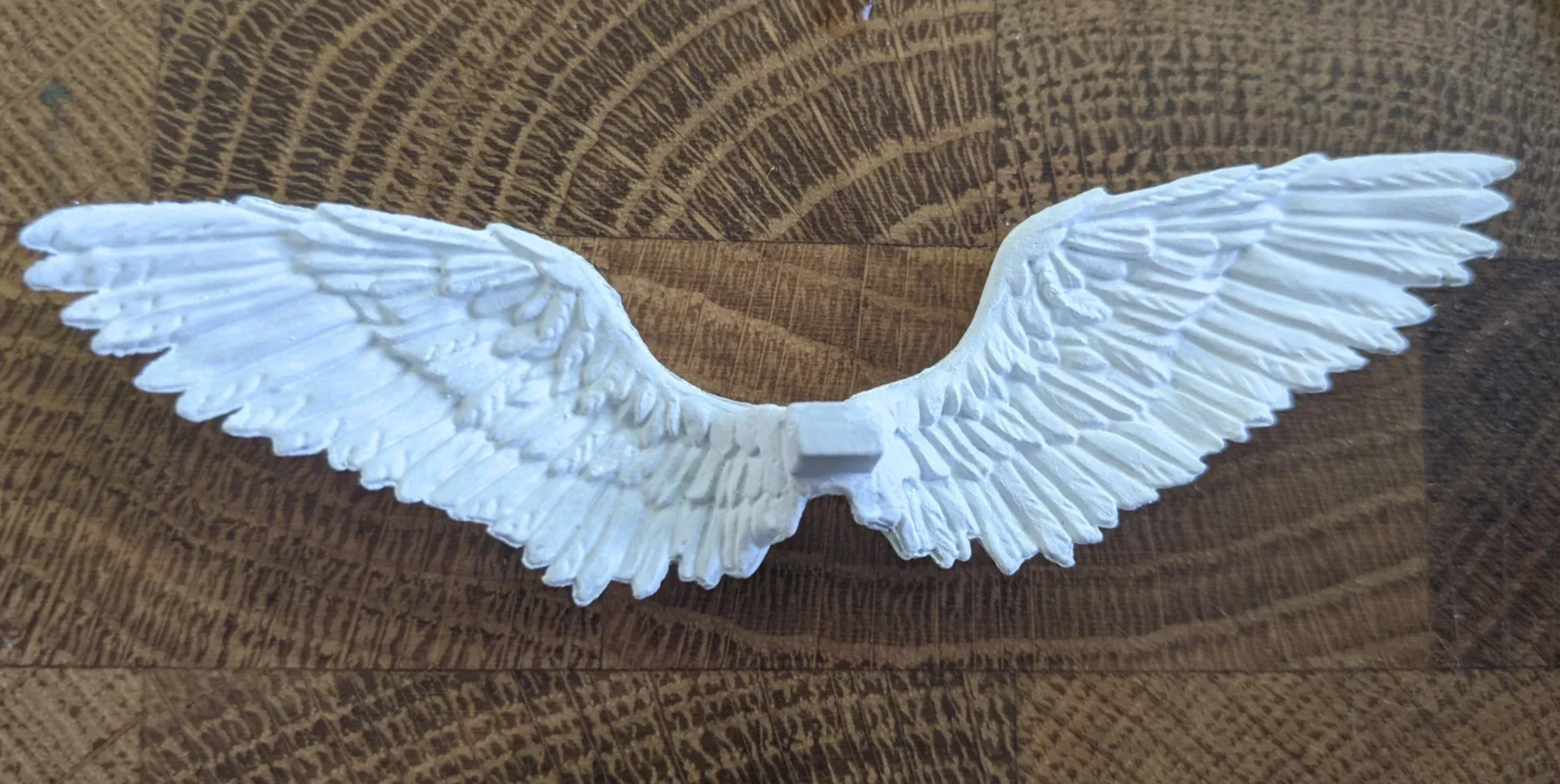 White, sculpted angel wings on a wood-grain surface.