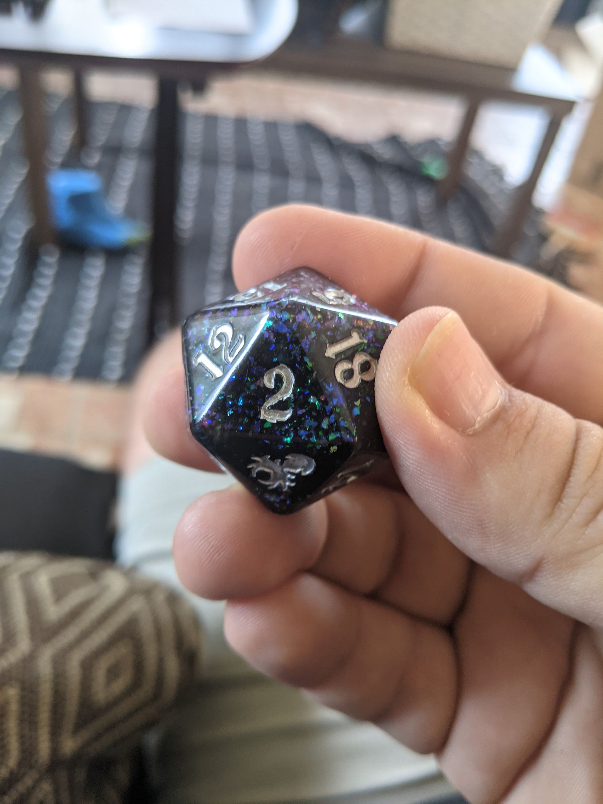 Hand holding a large, sparkly, black and blue D20 die with a