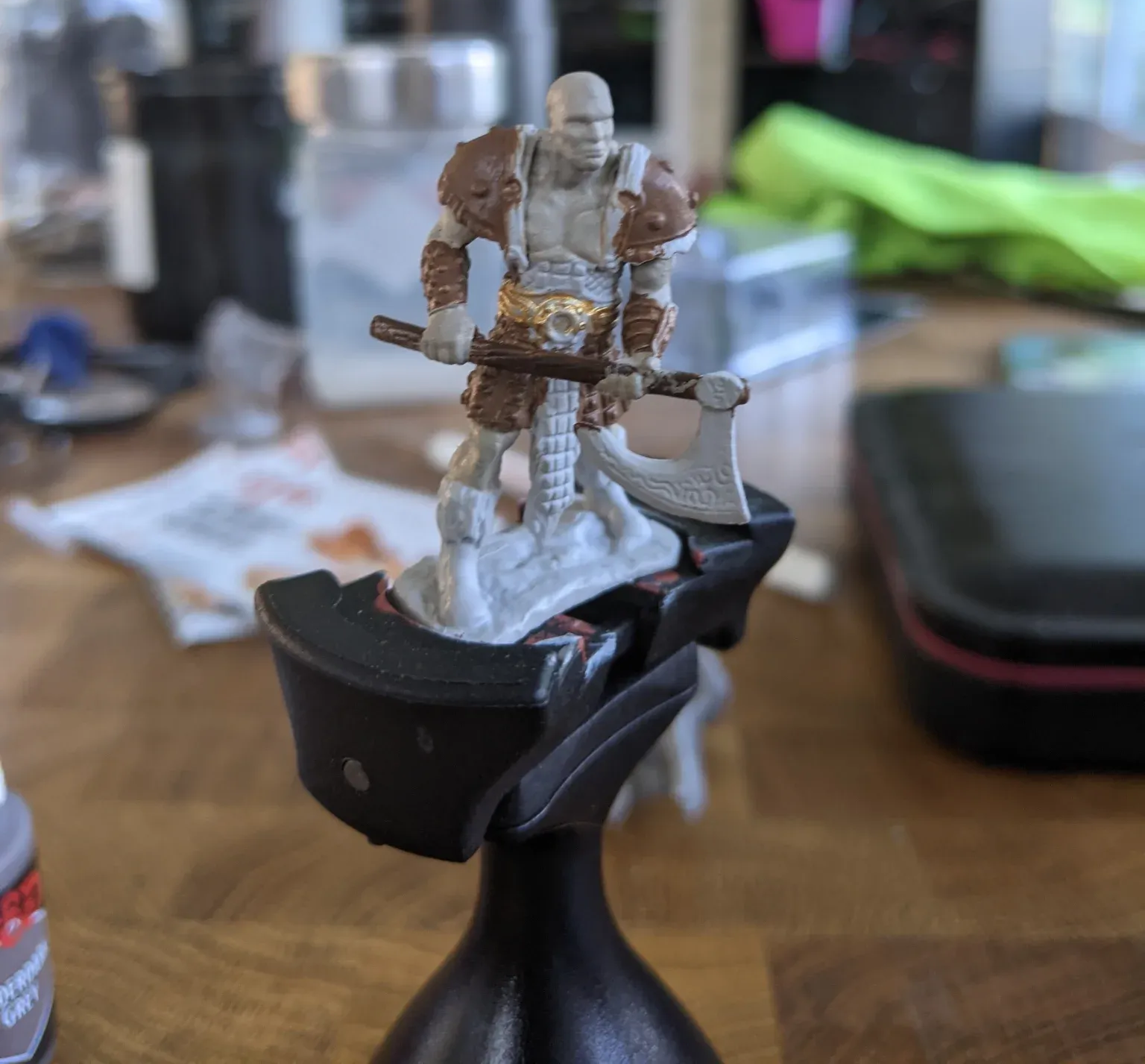 Miniature figure of a bald warrior with axe, painted brown, grey, and beige, on a black handle.