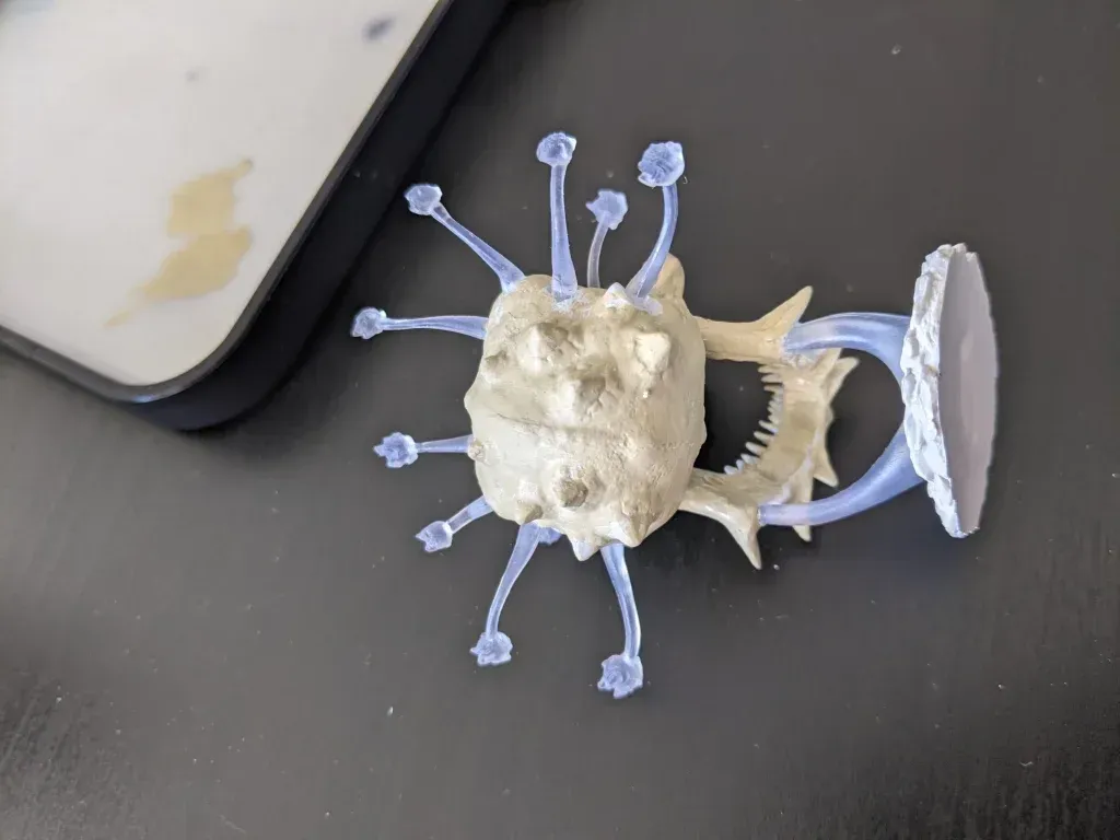 Gray, textured alien creature with blue tentacles, a jagged mouth, and attached to a base, next to a paint palette.