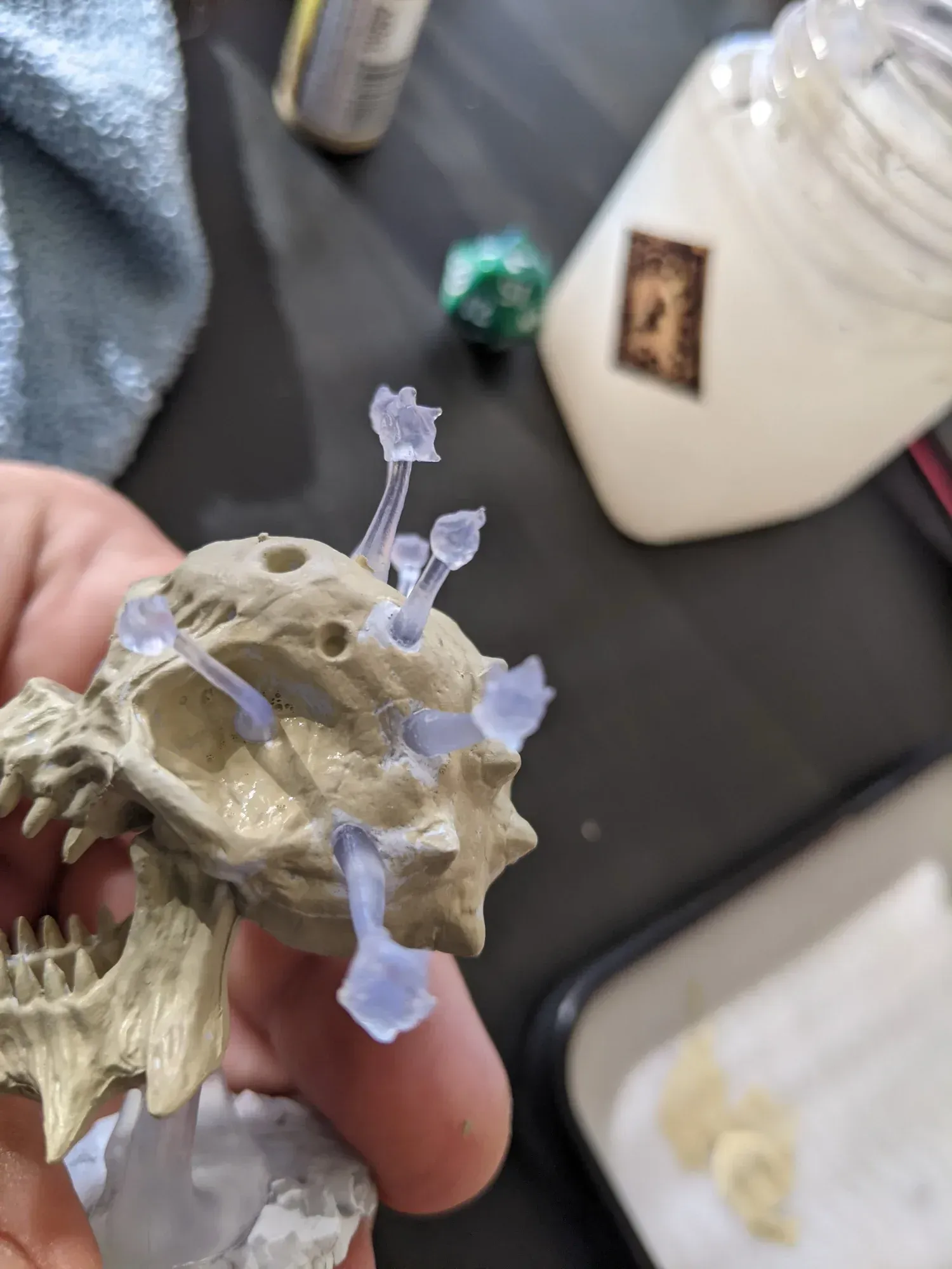 A skull miniature with translucent mushroom-like growths attached. The skull is off-white, held by a hand.