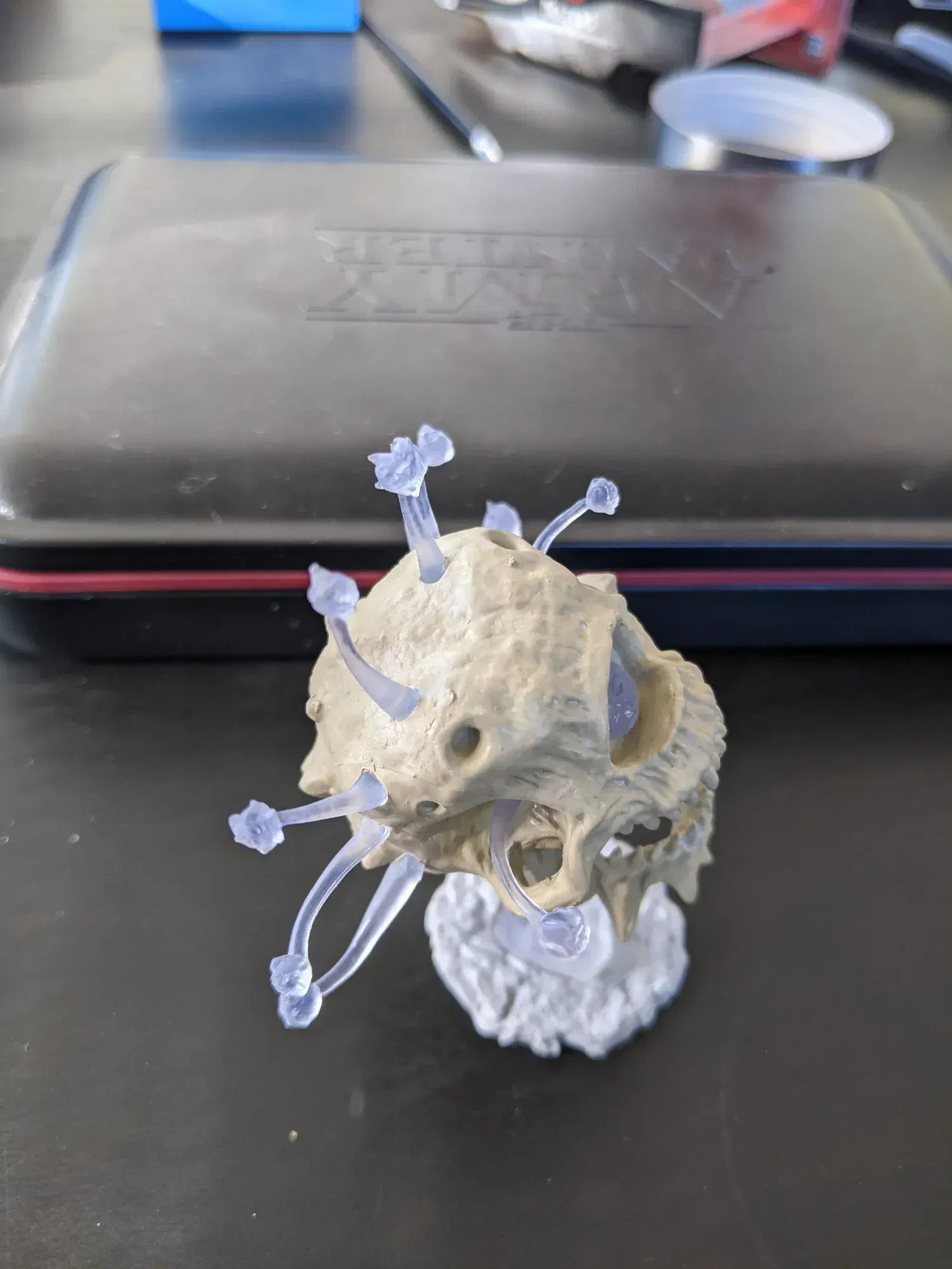 A small, tan model with clear, spiky appendages. It has a white base, set on a black surface.