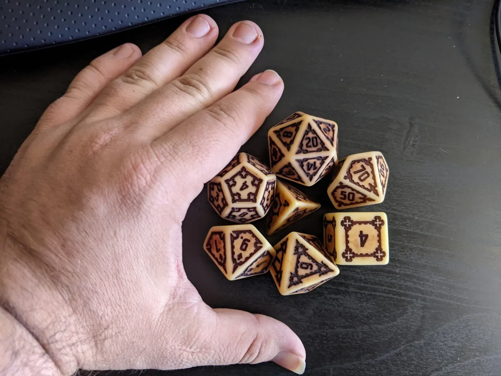 Hand next to a collection of tan and brown dice, likely used for tabletop games.
