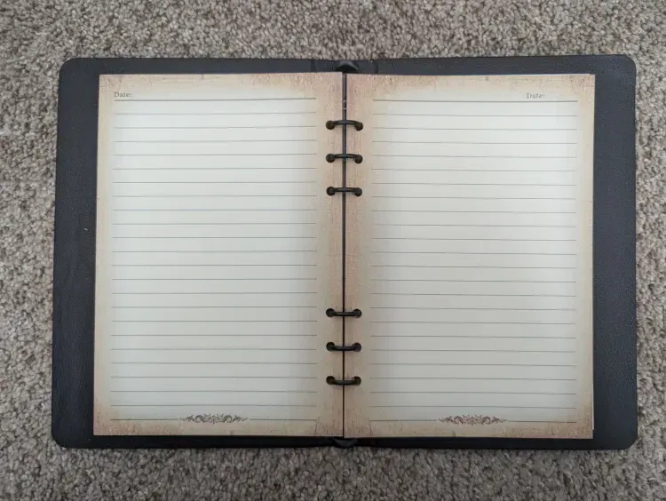 An open notebook with a black cover is sitting on a carpet.