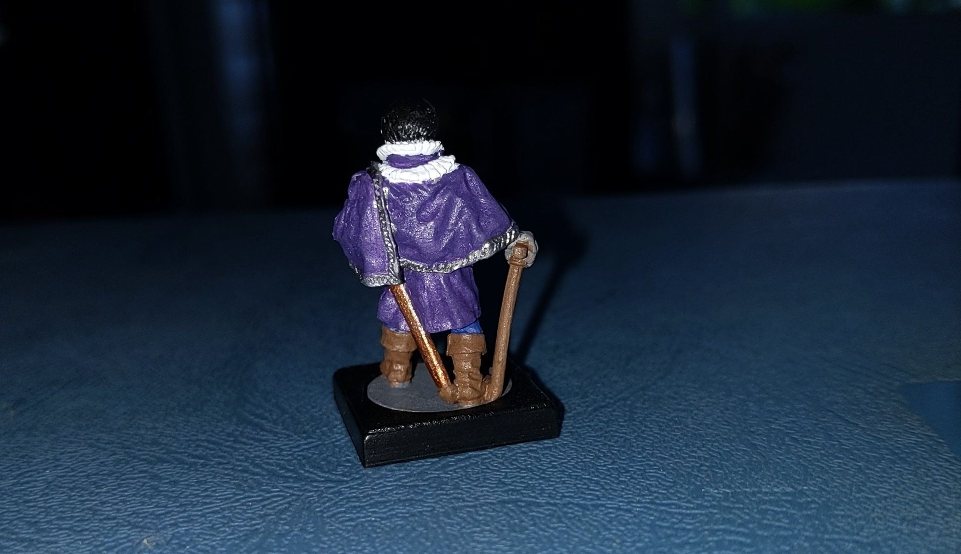 Miniature figure of a person in purple robes, holding a staff on a black base.