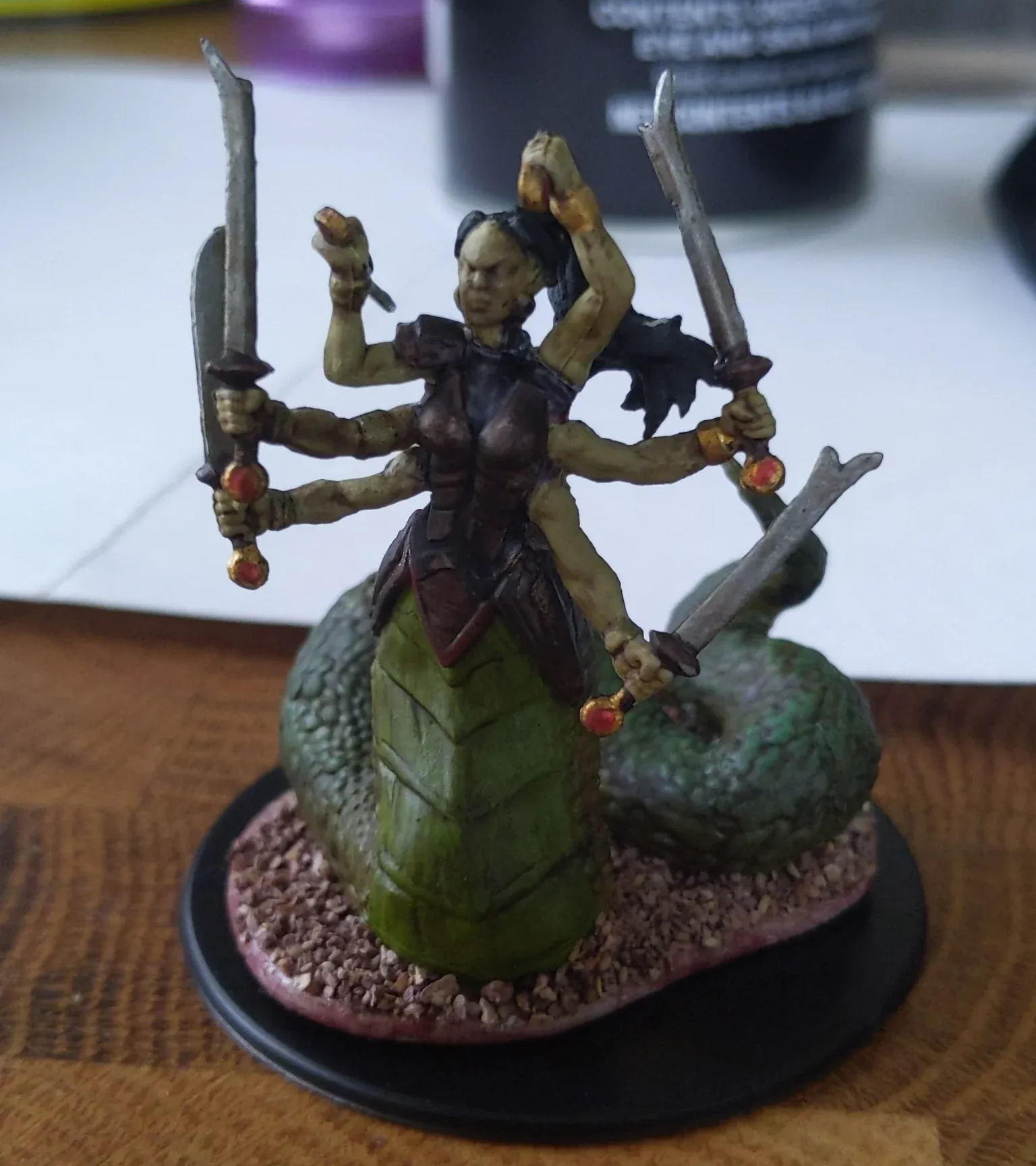 A multi-armed naga miniature figure with swords, snake lower body, holding weapons, on a base.