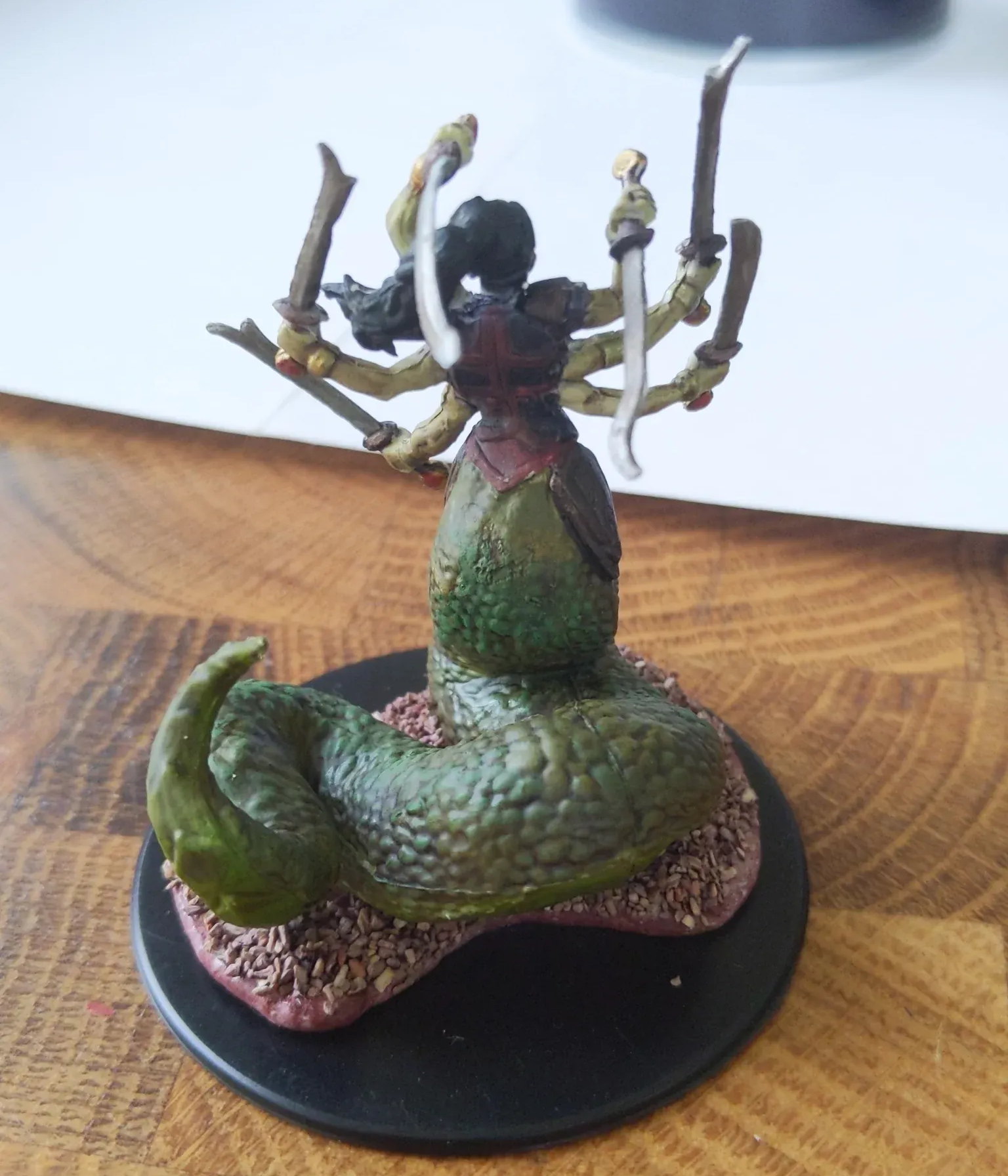 A miniature painted figure of a multi-armed woman with a serpentine lower body, holding swords on a black base.