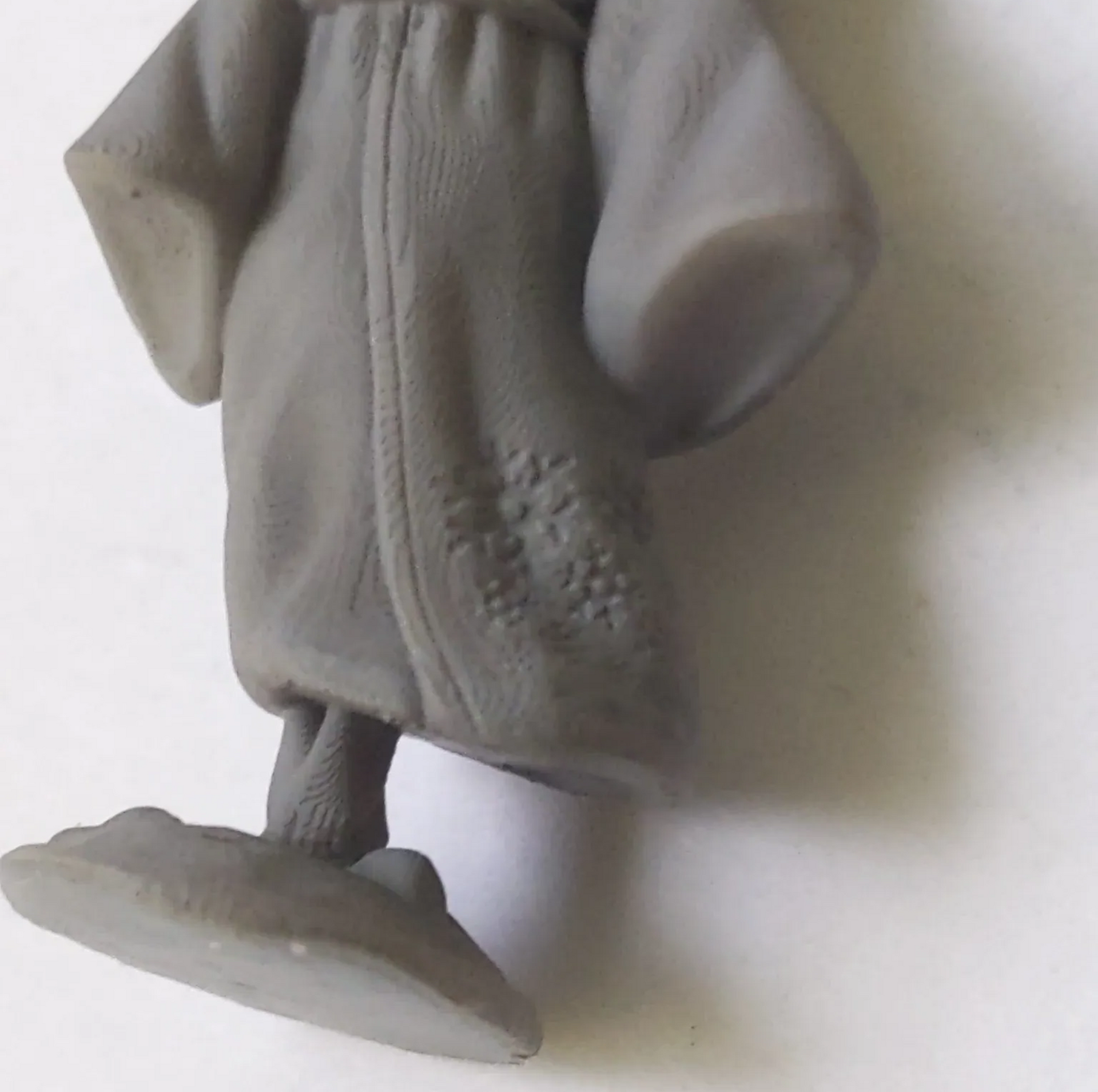 Close-up of a gray figure, wearing robes, standing on a platform, with intricate details on the robe.