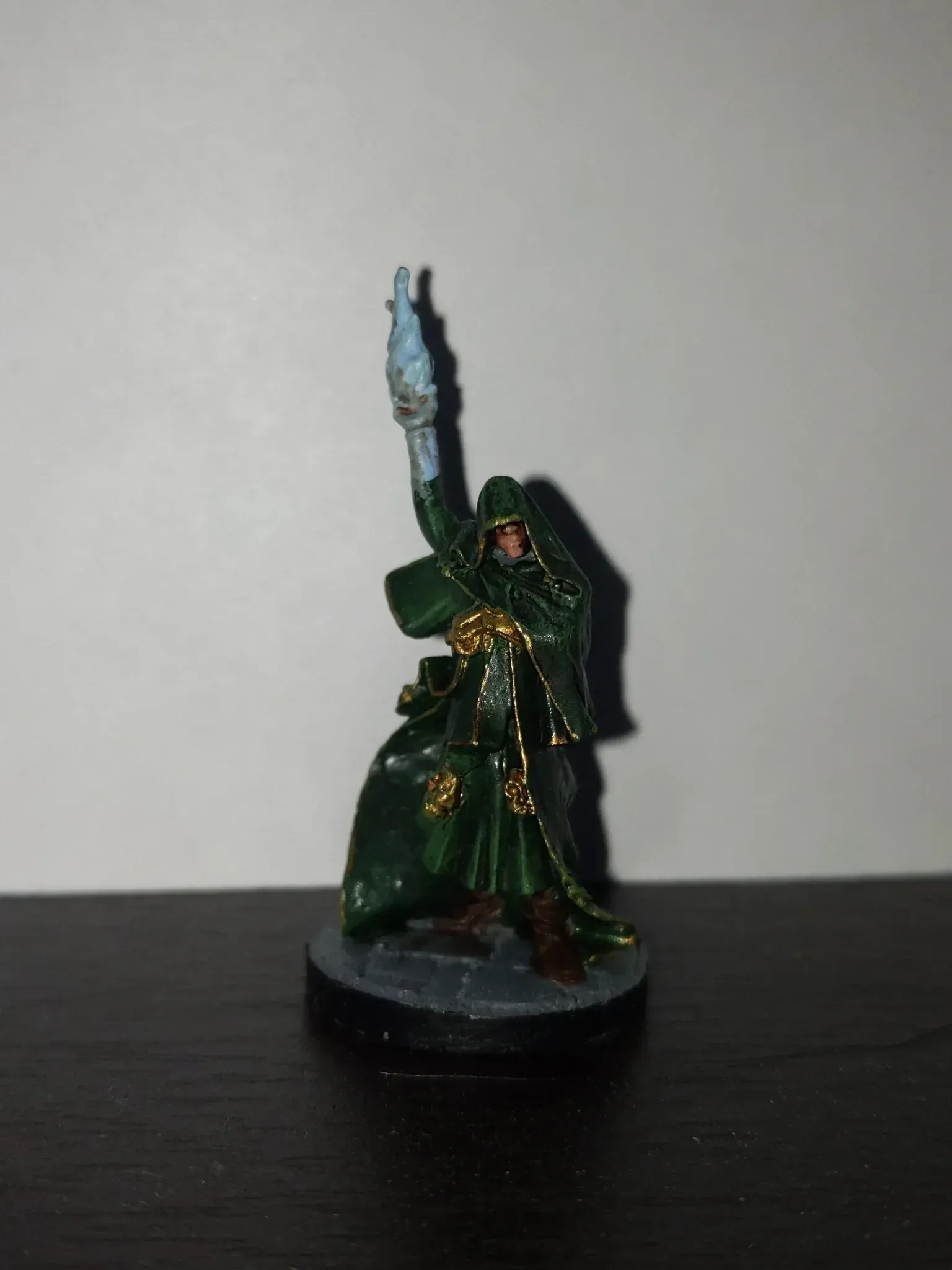 Miniature figure of a robed wizard in green, holding up a staff with blue energy.