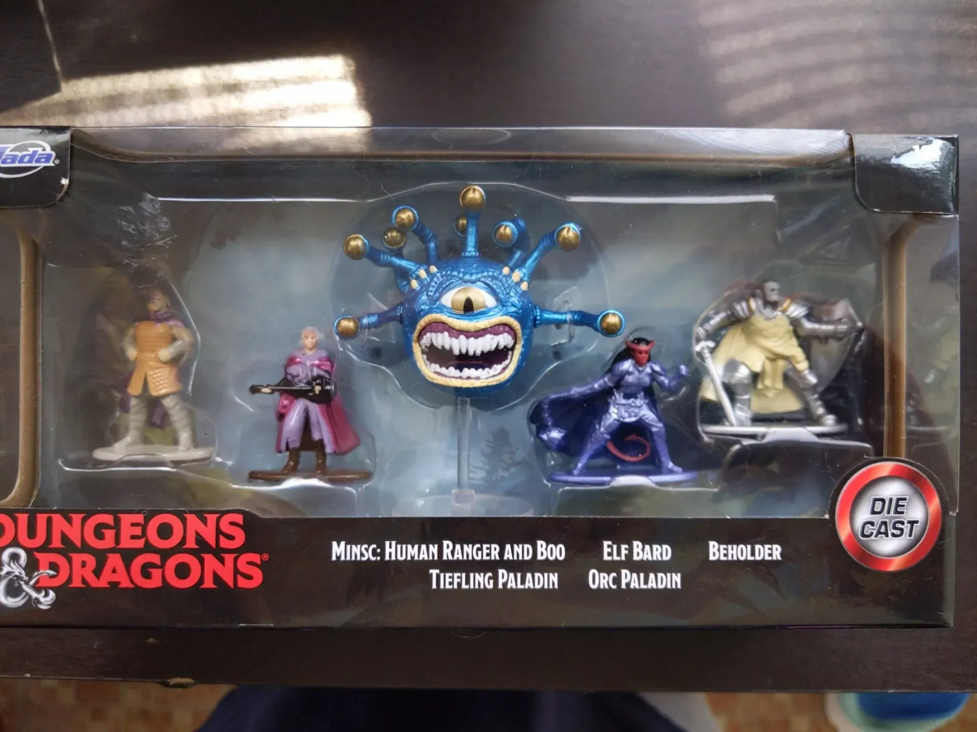 D&D miniatures set: Human, Beholder, Elf, Humanoid, & a figure with armor. Black box with red logo.