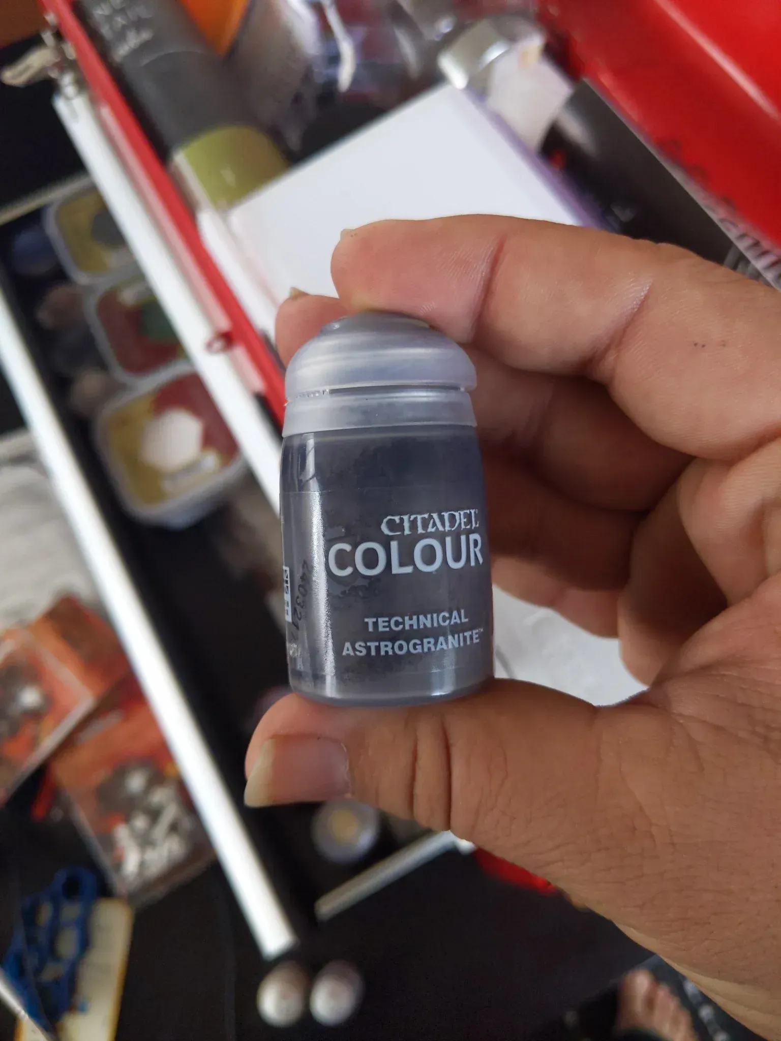 A person's hand holding a small, gray Citadel paint pot. The label reads