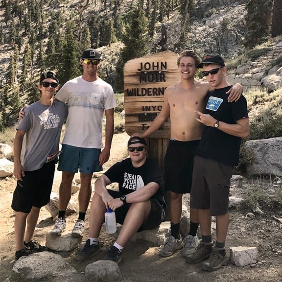 A group of young men are posing for a picture in front of a wooden sign that says john muir wilderness