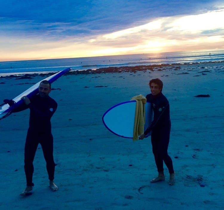 Two men carrying surfboards on a beach at sunset