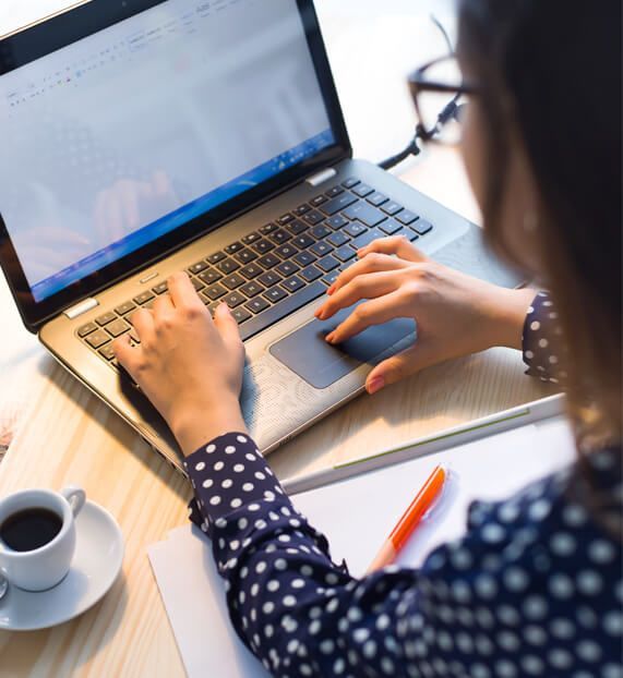 A woman is typing on a laptop next to a cup of coffee