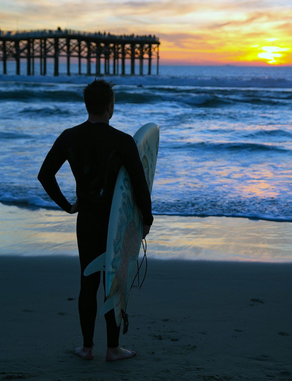 A man holding a surfboard on a beach at sunset