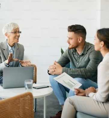 A woman is talking to a man and a woman while sitting at a table with a laptop.