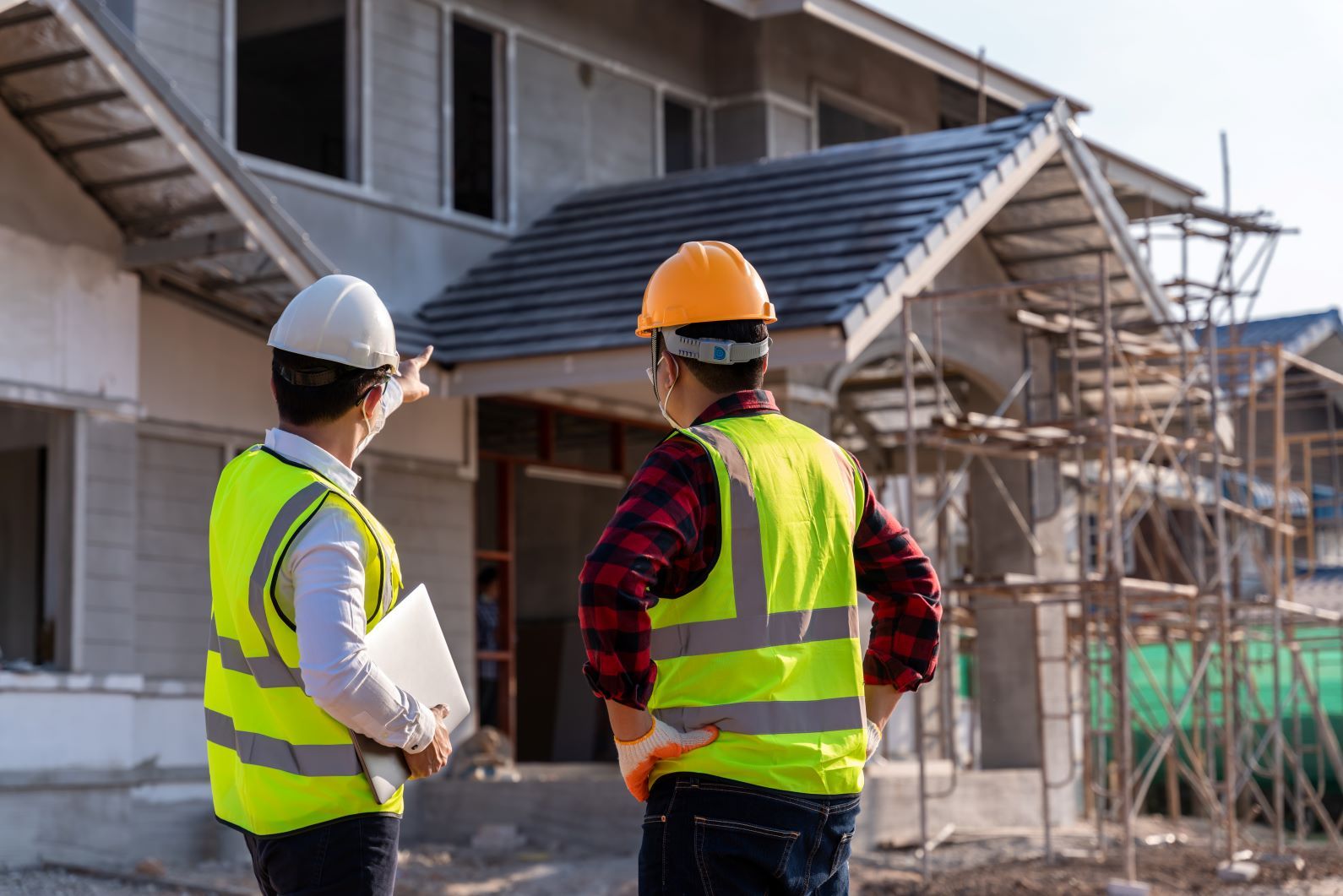Two Construction Workers Are Standing In Front Of A House Under Construction