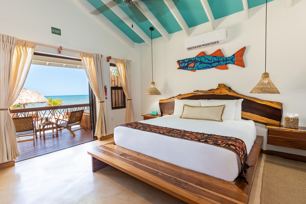 Bright beach bungalow bedroom with white bed, turquoise beams, and ocean-view balcony