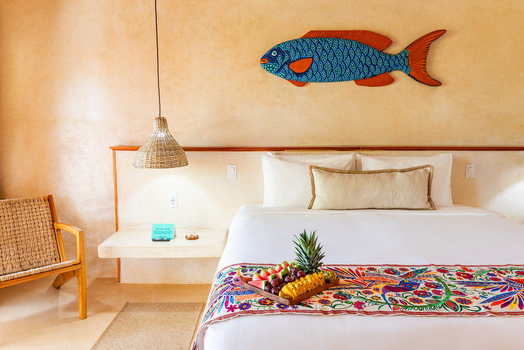 Bright bedroom with a white bed, woven chair, hanging lamp, and colorful fish wall art