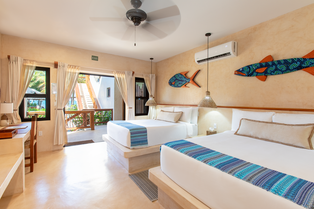 Bright beachfront bedroom with two beds, blue accents, and open doors to a patio and ocean view