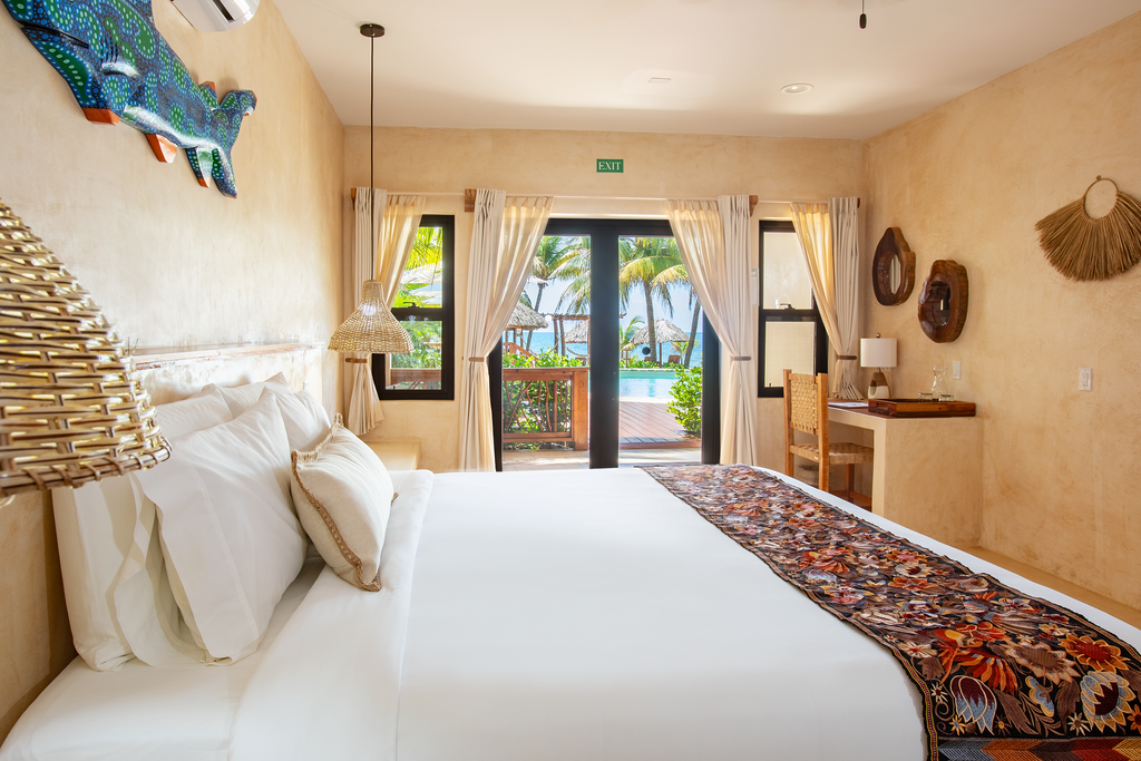 Bright beach-style bedroom with white bed, woven decor, and open doors to a patio and garden.
