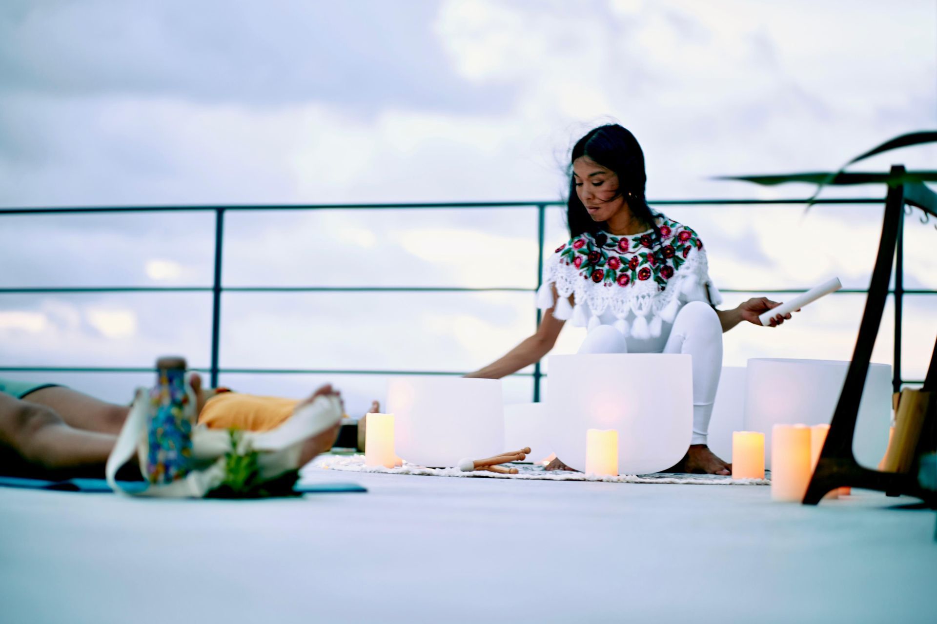 Woman arranging candles on a rooftop table at sunset, with dinner items and a railing in the background