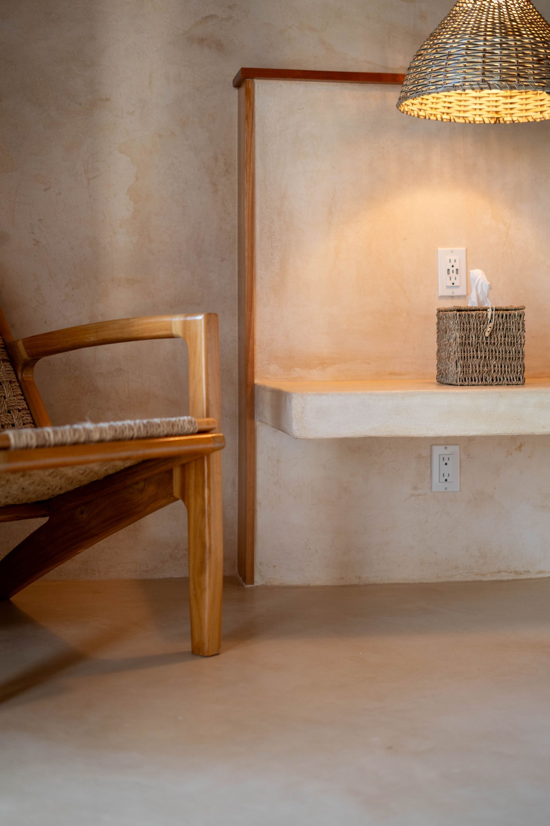 Modern corner with wooden chair, white bench shelf, woven pendant lamp, and electrical outlet on textured wall