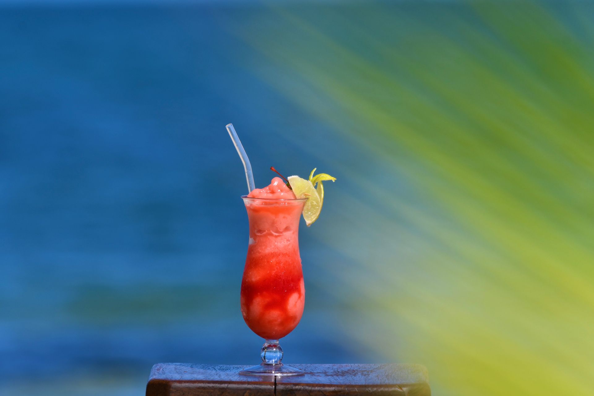 Red cocktail with straw and lime garnish on a bar against a blue-yellow background