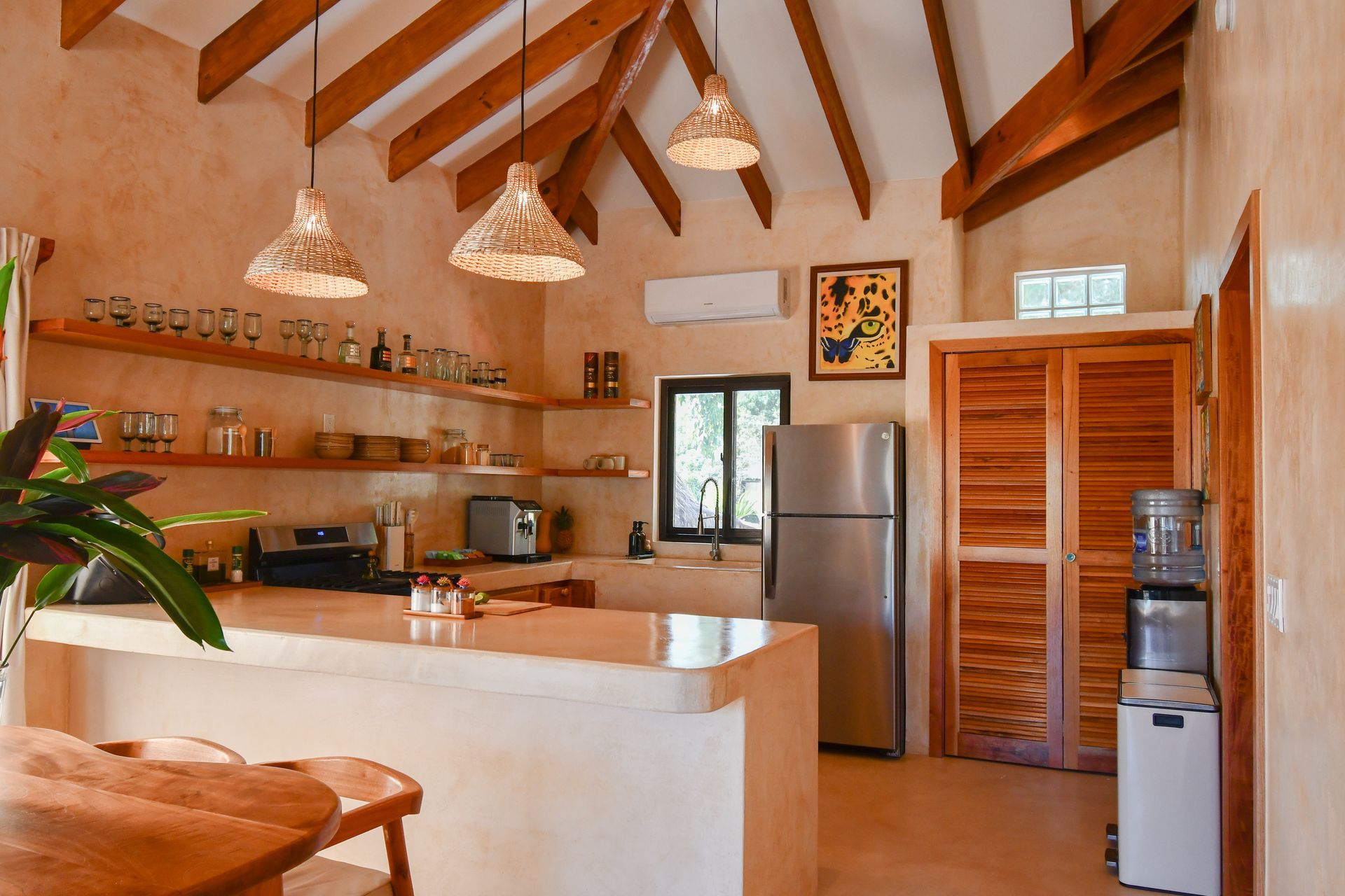 Bright, modern kitchen with white island, wood beams, hanging lights, and stainless-steel fridge.