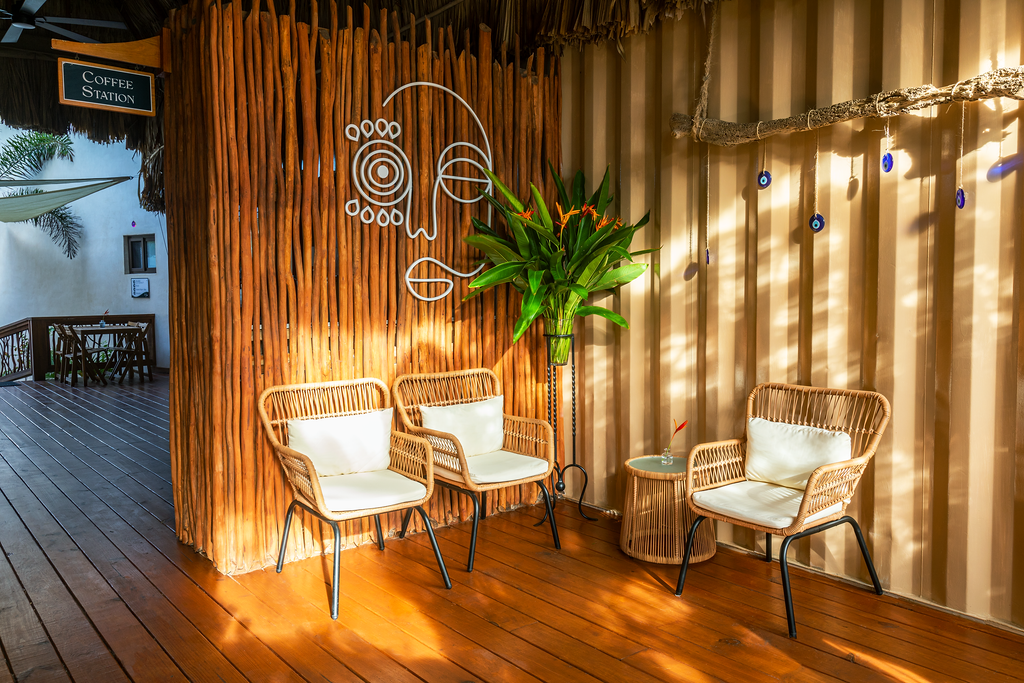 Cozy sunlit lounge with wicker chairs, wooden floor, and tropical plant behind a curtain wall