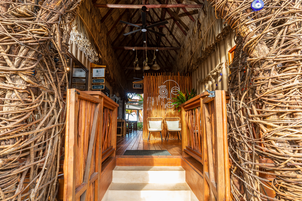 Rustic wooden walkway inside a thatched hut with woven walls and benches at the end