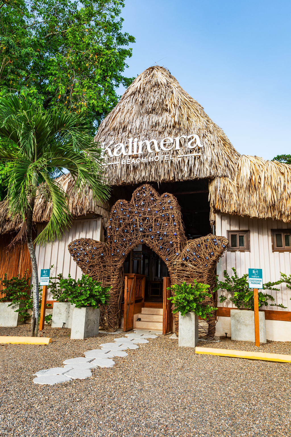 Thatched building entrance with a star-shaped wood facade, white path, and greenery under a blue sky