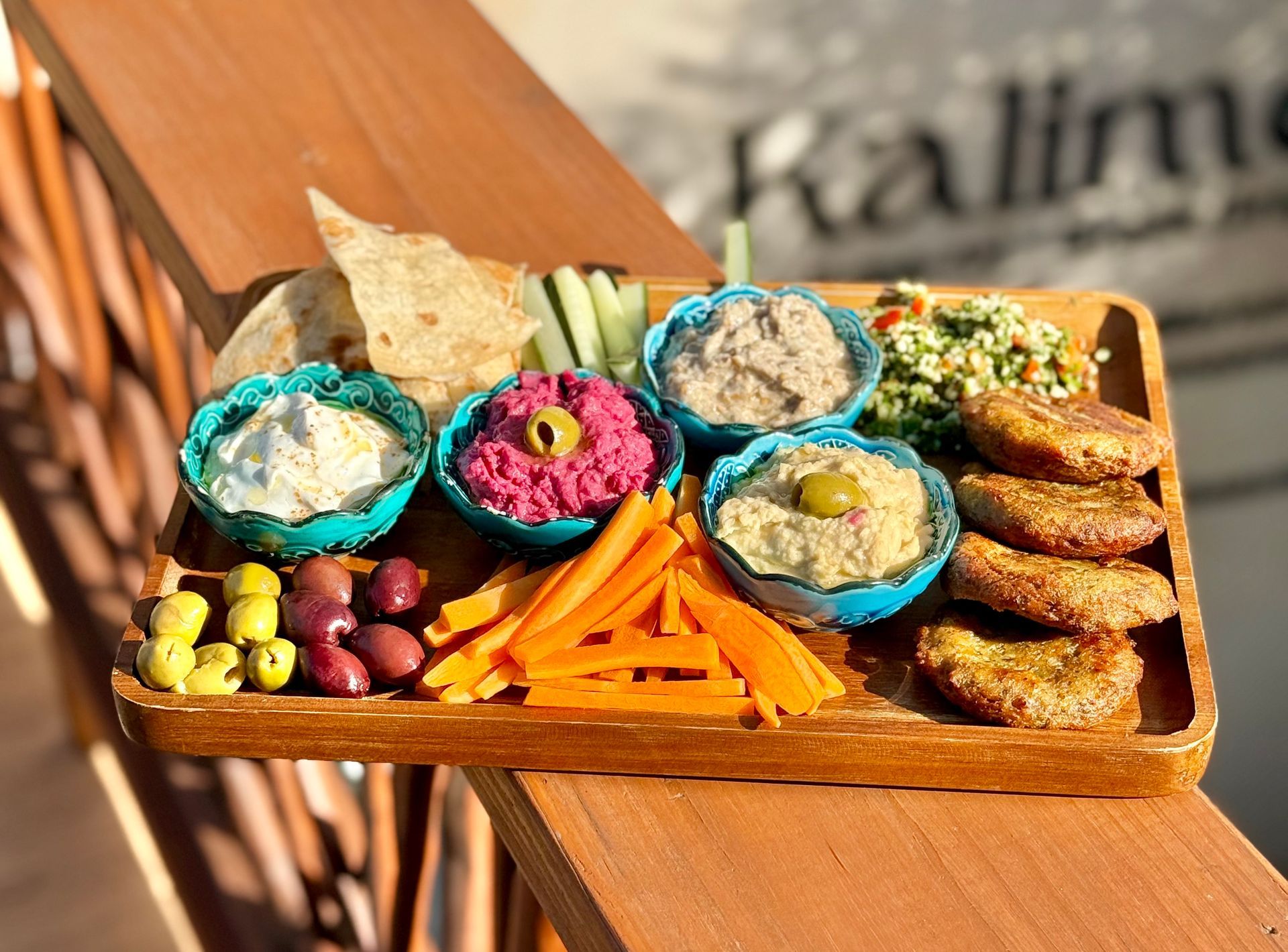 Assorted colorful Indian snacks served on a wooden tray outdoors, with chutneys and vegetables