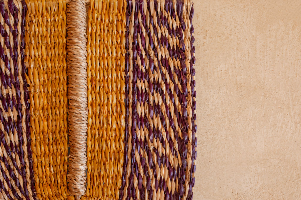 Close-up of woven yarn strands in orange, purple, and beige beside a plain tan surface