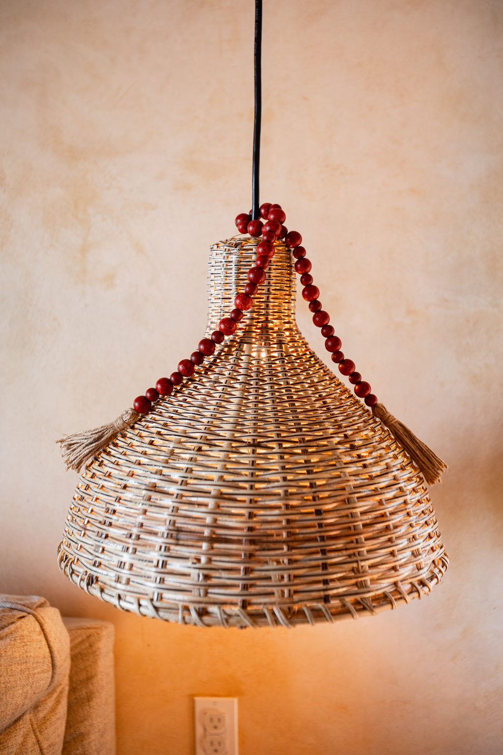 Woven hanging pendant lamp with red bead trim against a beige wall