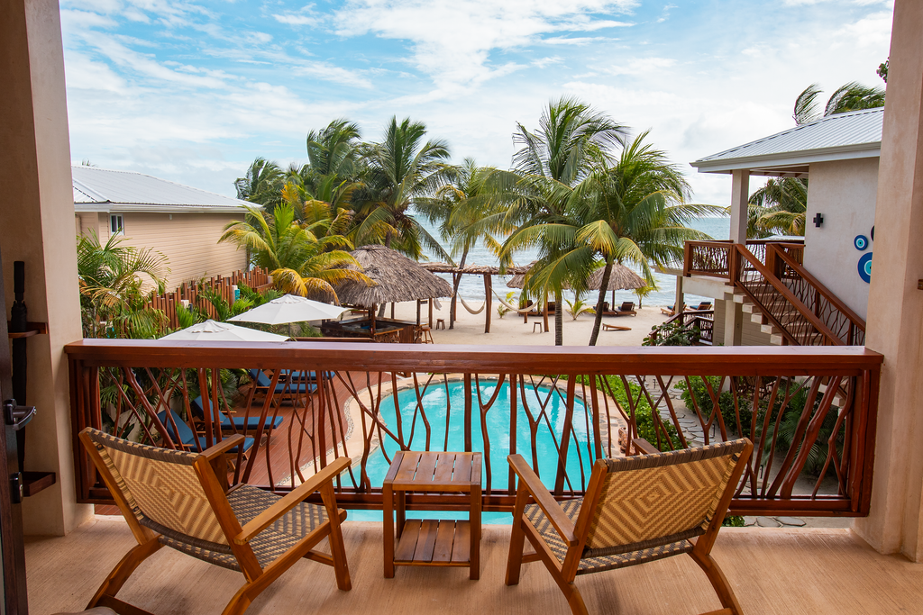 Resort balcony with two wicker chairs overlooking a turquoise pool and palm trees