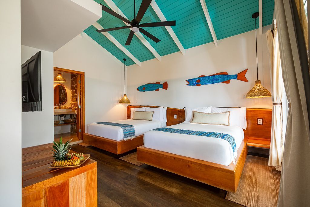 Bright bedroom with two beds, teal ceiling, pendant lights, and wooden floor; warm, airy decor